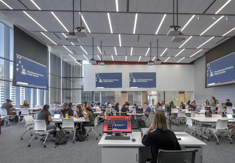 An image of a large open lecture room with a lot of people seated at various desks.