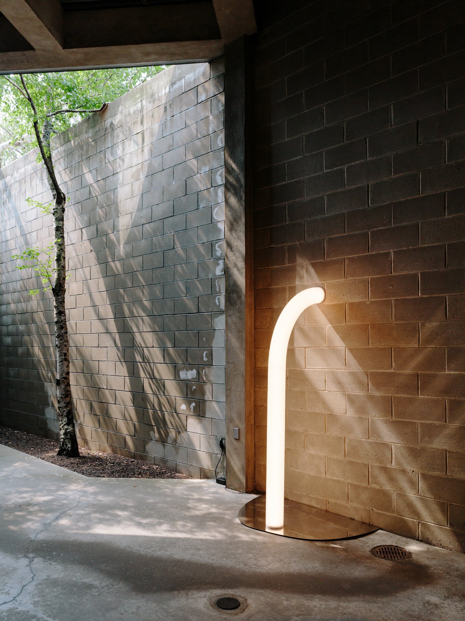 A tube light sculpture by Objects of Common Interest on a mirrored surface on the concrete floor of an outdoor gallery at the Isamu Noguchi Museum. 