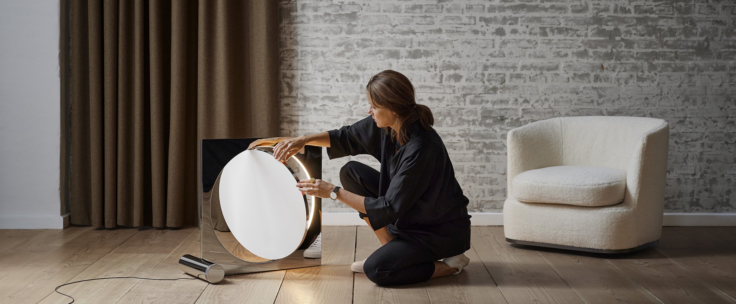 Anne Boysen manipulating a lamp she designed. one of her armchairs is in the background.