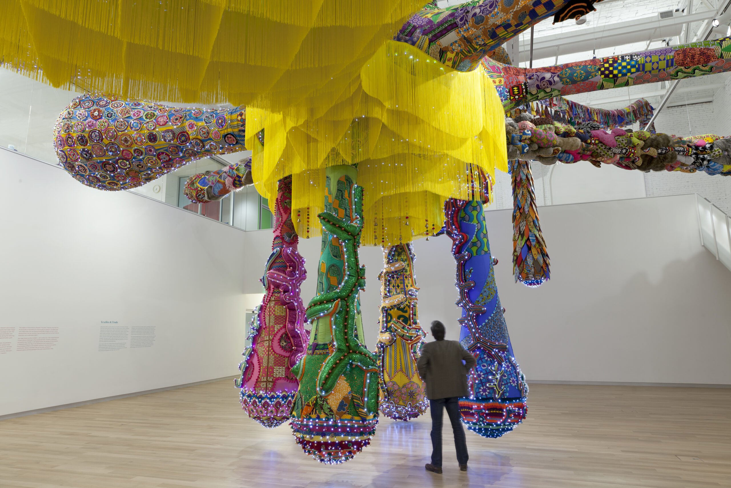 An image of a massive textile installation with a person standing under it in a white walled gallery