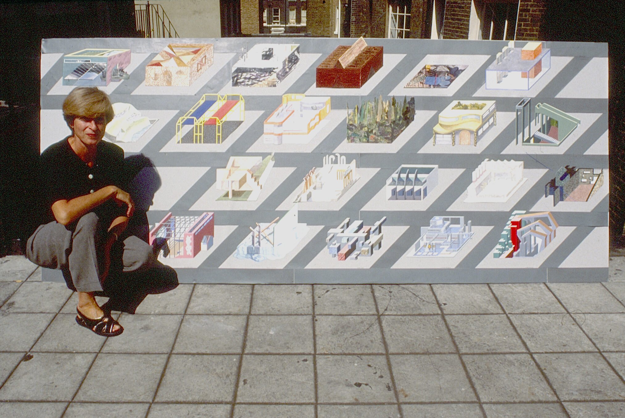 Photograph of a woman presenting a large board of student architecture work