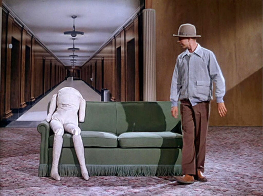 man standing in front of a sofa with a dummy on it. 