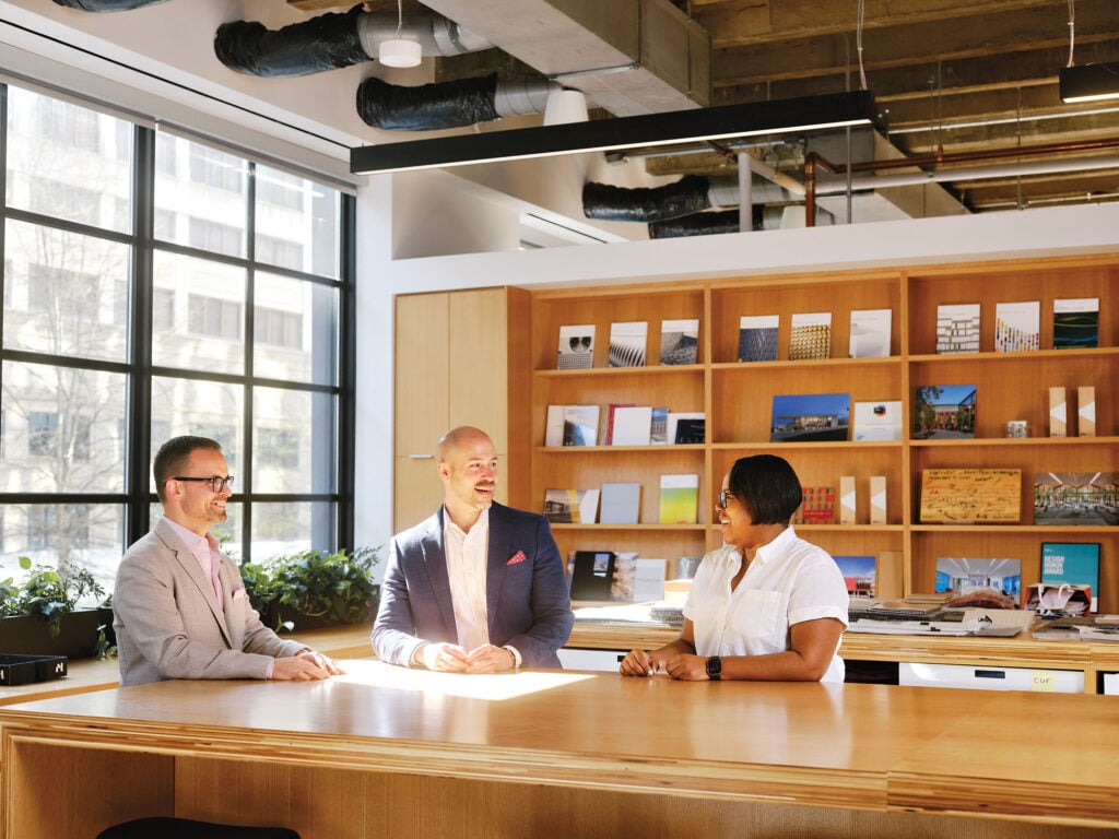 three people sitting at a conference table in an architecture studio