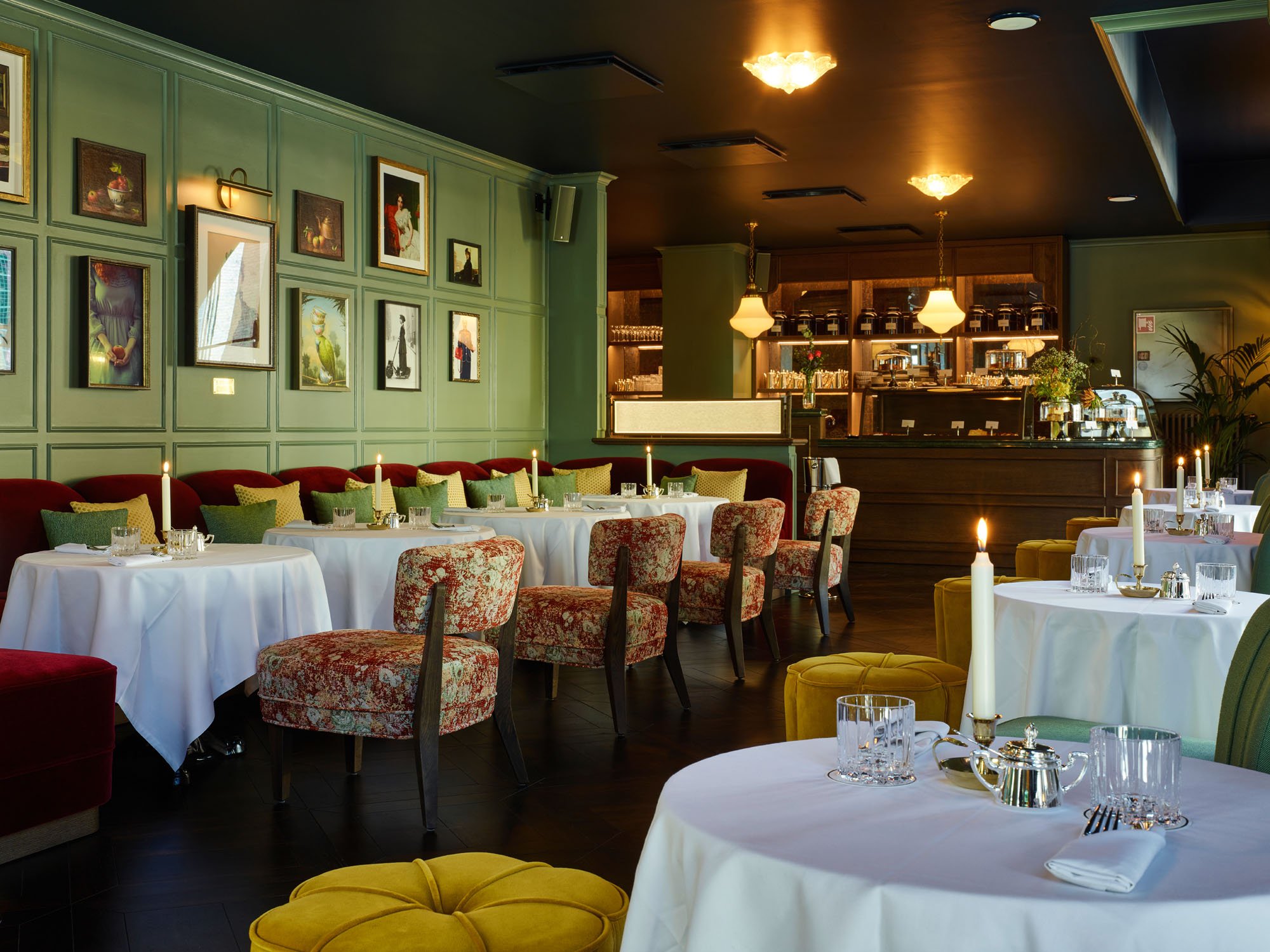 hotel restaurant in shades of green with uphilstered chairs and white table cloths. 