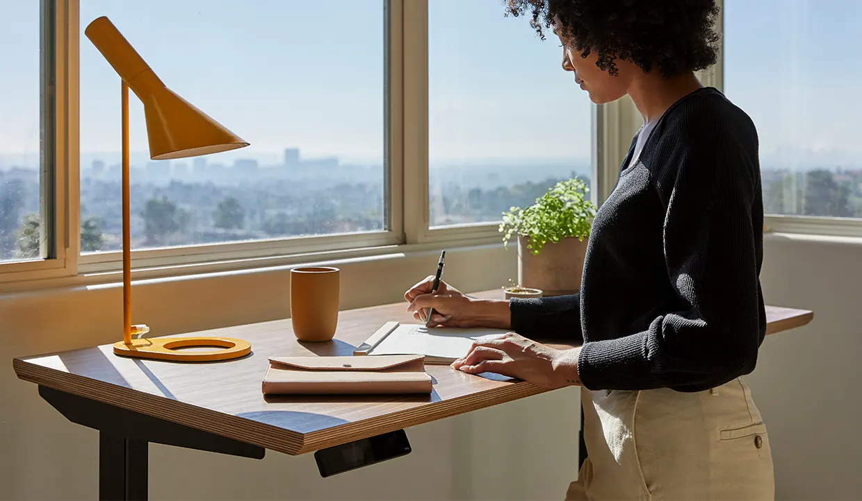 Woman writes at a high desk. 