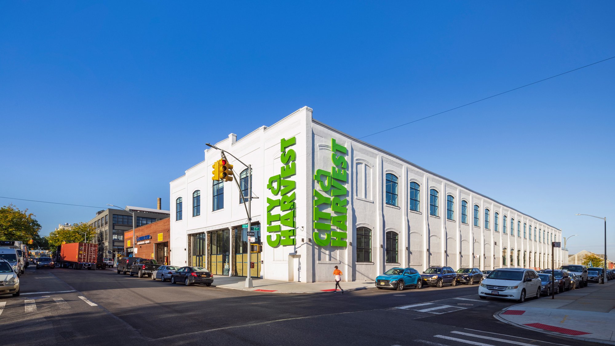 a photograph of the exterior of a whitewashed industrial building with the city harvest logo in green on its side