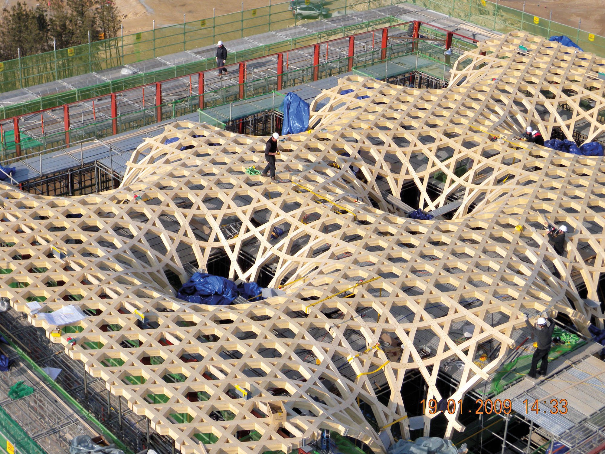 workers standing on the top of a wooden gridshell structure designed by Shigeru Ban