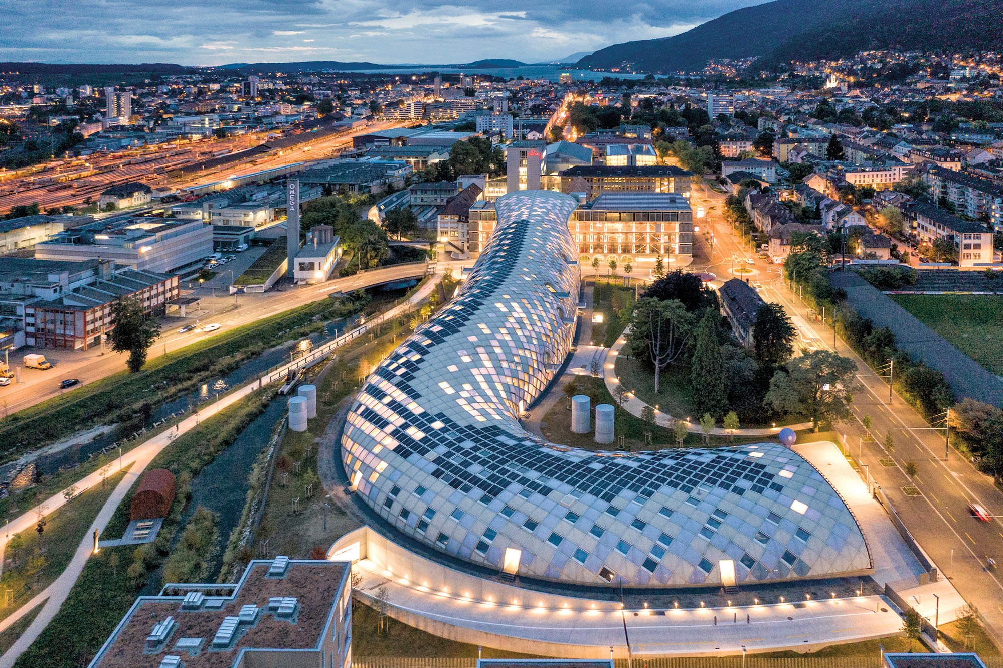 an aerial view of the swatch headquarters in Biel Switzerland, a serpentine shaoped building with a checkerboard pattern of windows and solar panels