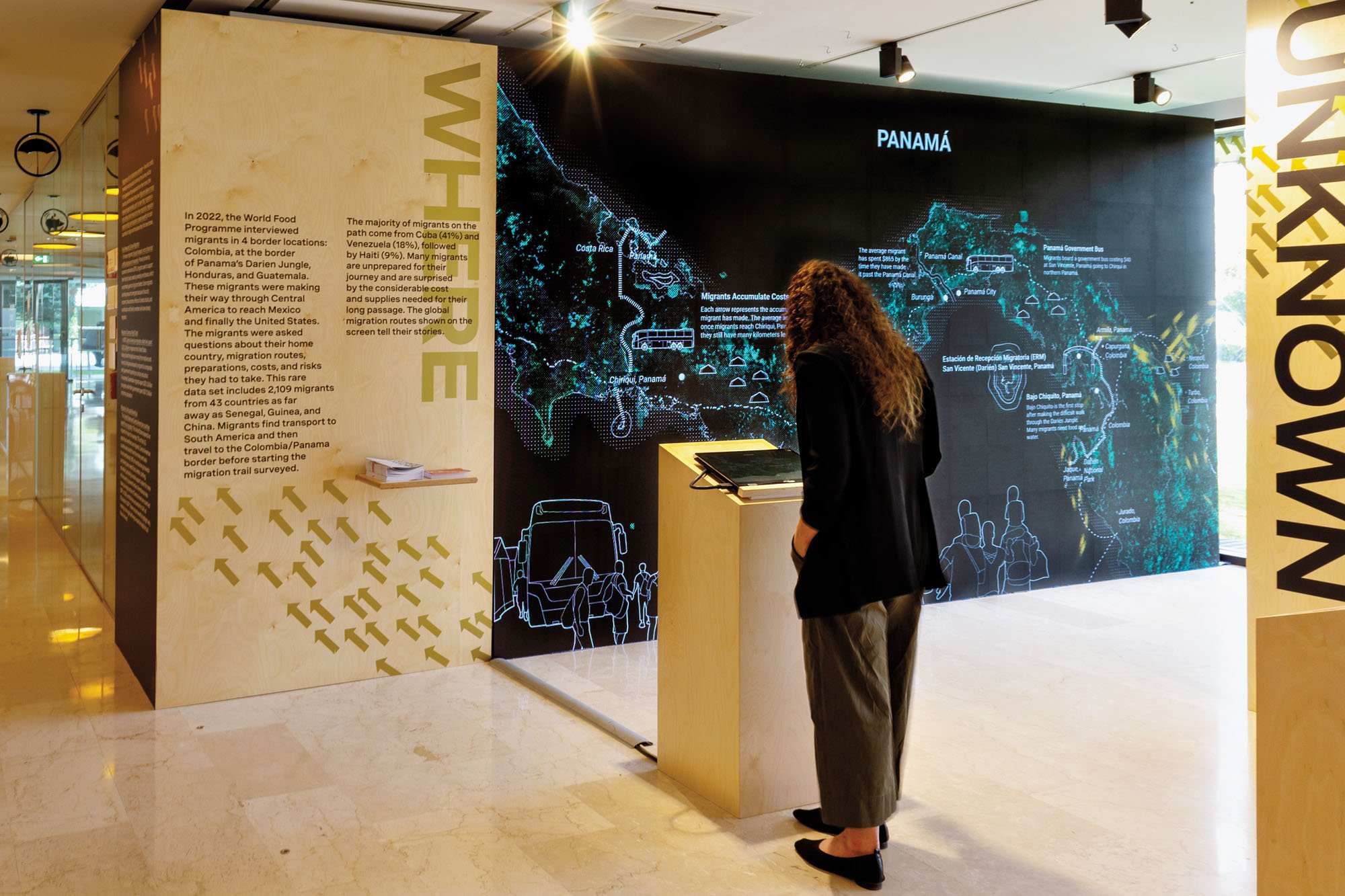 a person standing in an exhibition hall  at MIT's Civic Data Design Lab in front of a map about migration data