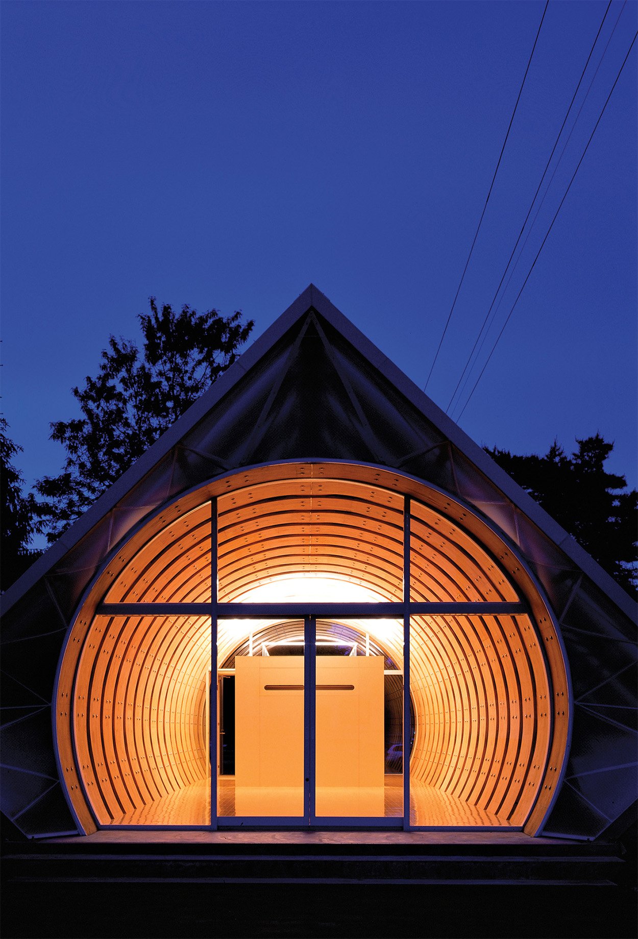 the exterior of the imai hospital daycare center by shigeru ban in the evening show a circular interior form with LVL boards