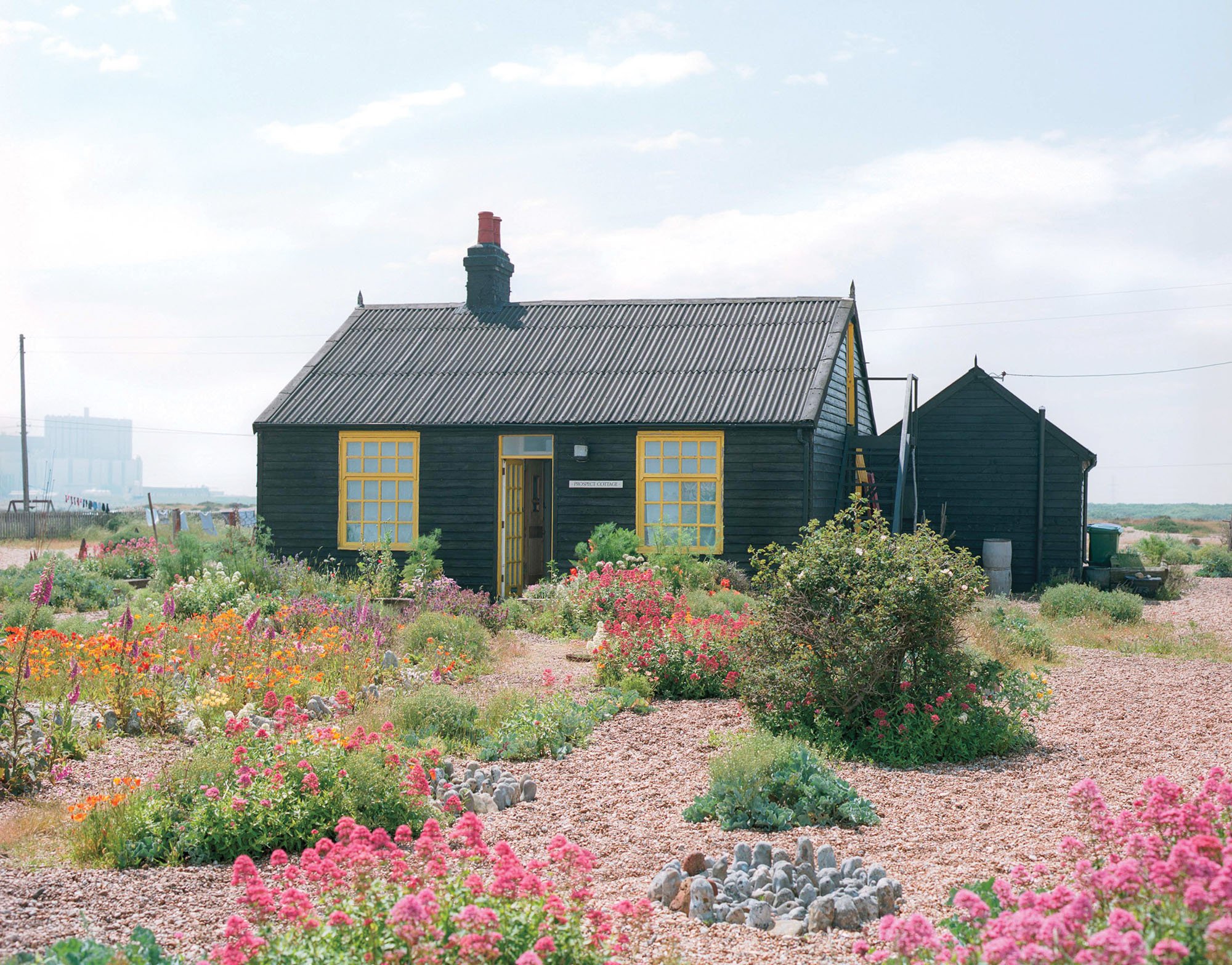 a black cottage surrounded by a colorful garden and stones