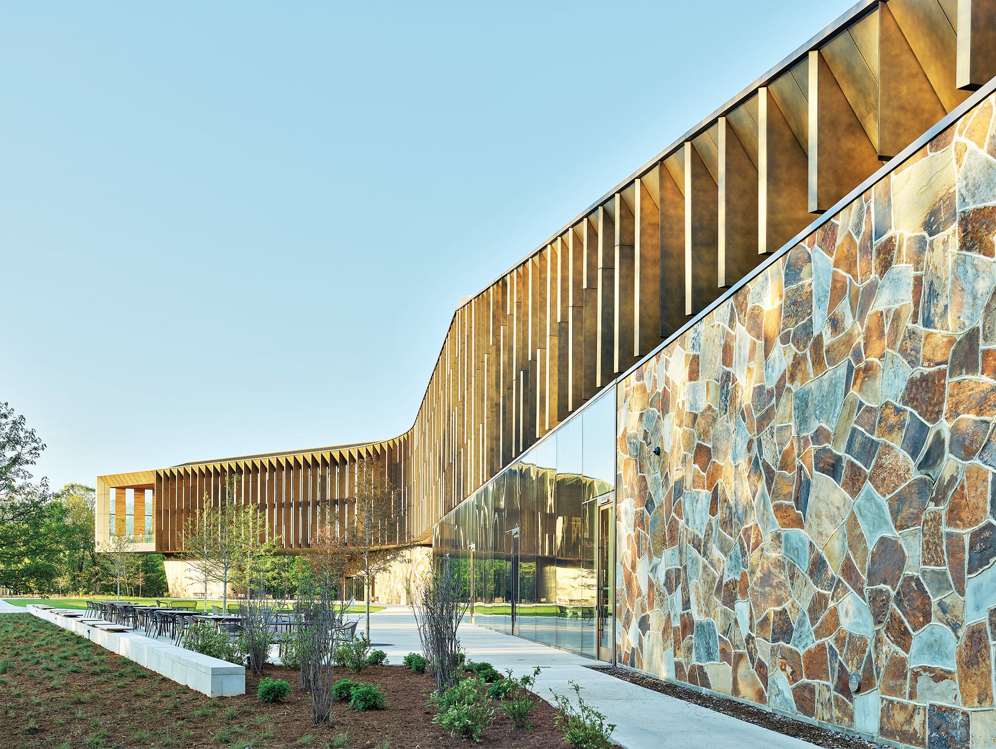 An exterior of the vernacular building made with copper facade, glass walls and and giraffe stone walls.