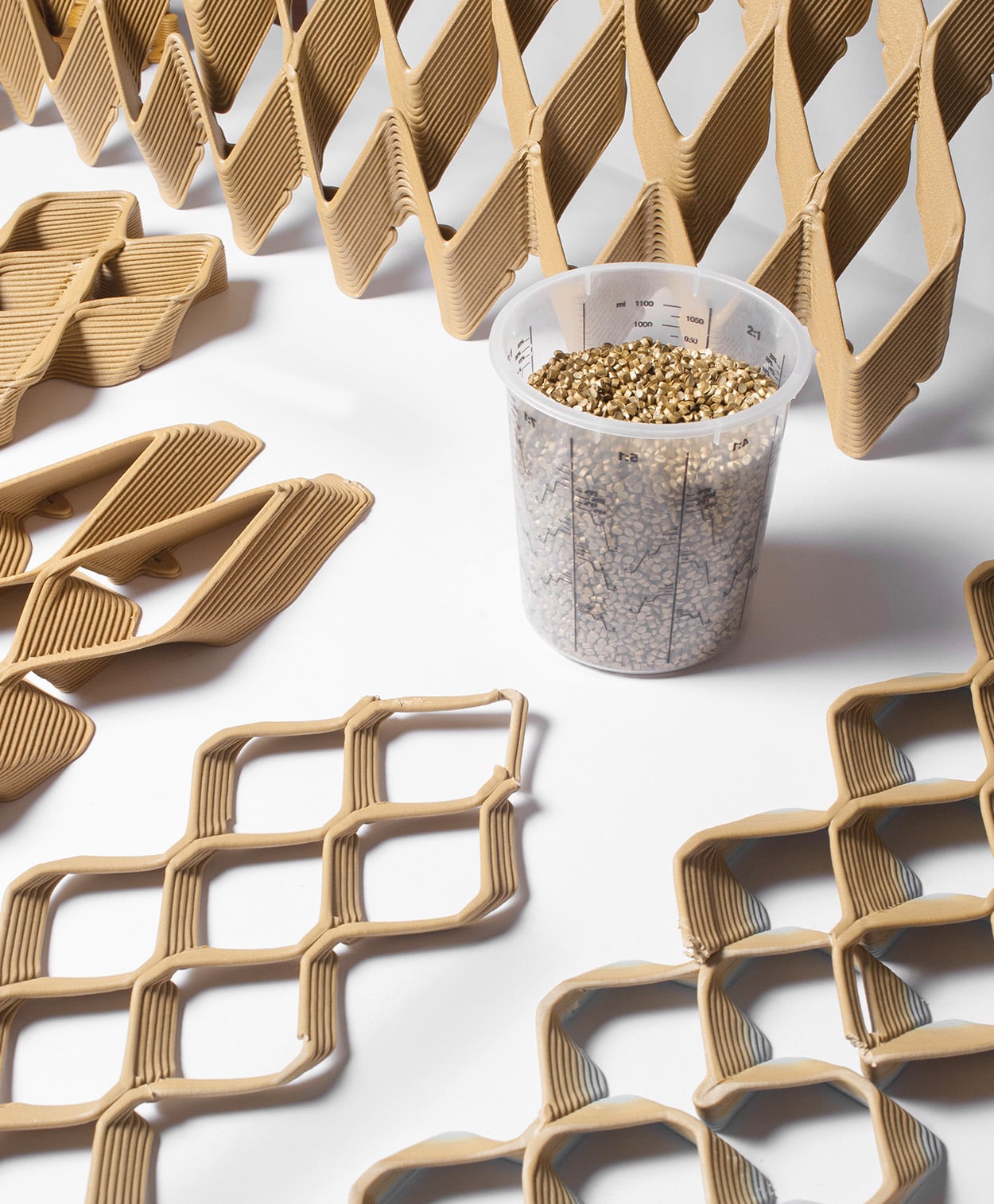 Waste pellet like material kept in a measuring glass alongside the 3D printed model structure of the facade wall in different origami patterns. 