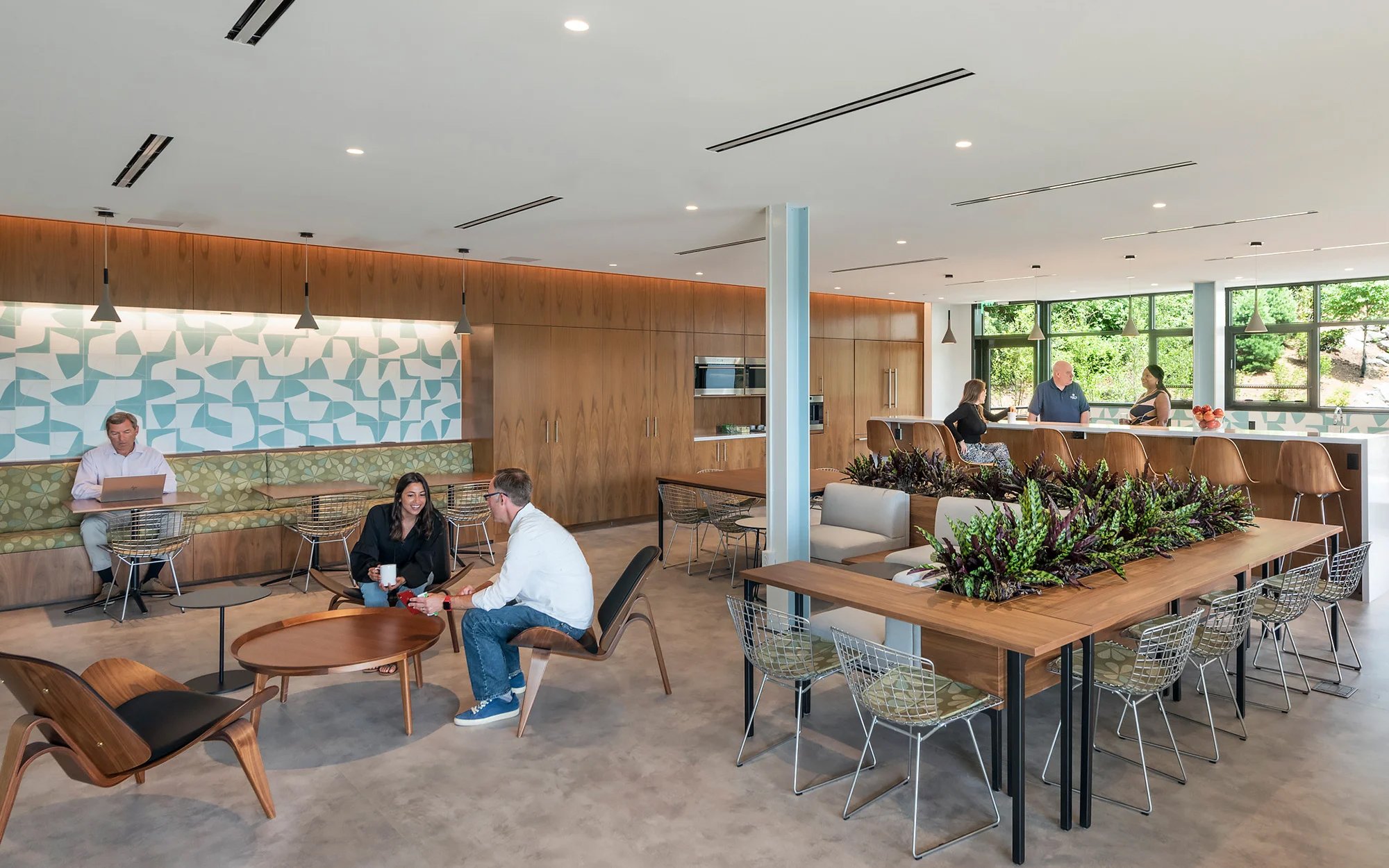 Interiors of the HTMX building with plants on the table and people sitting and chatting on the lounge chairs, working on the back and also sitting around the kitchen area.