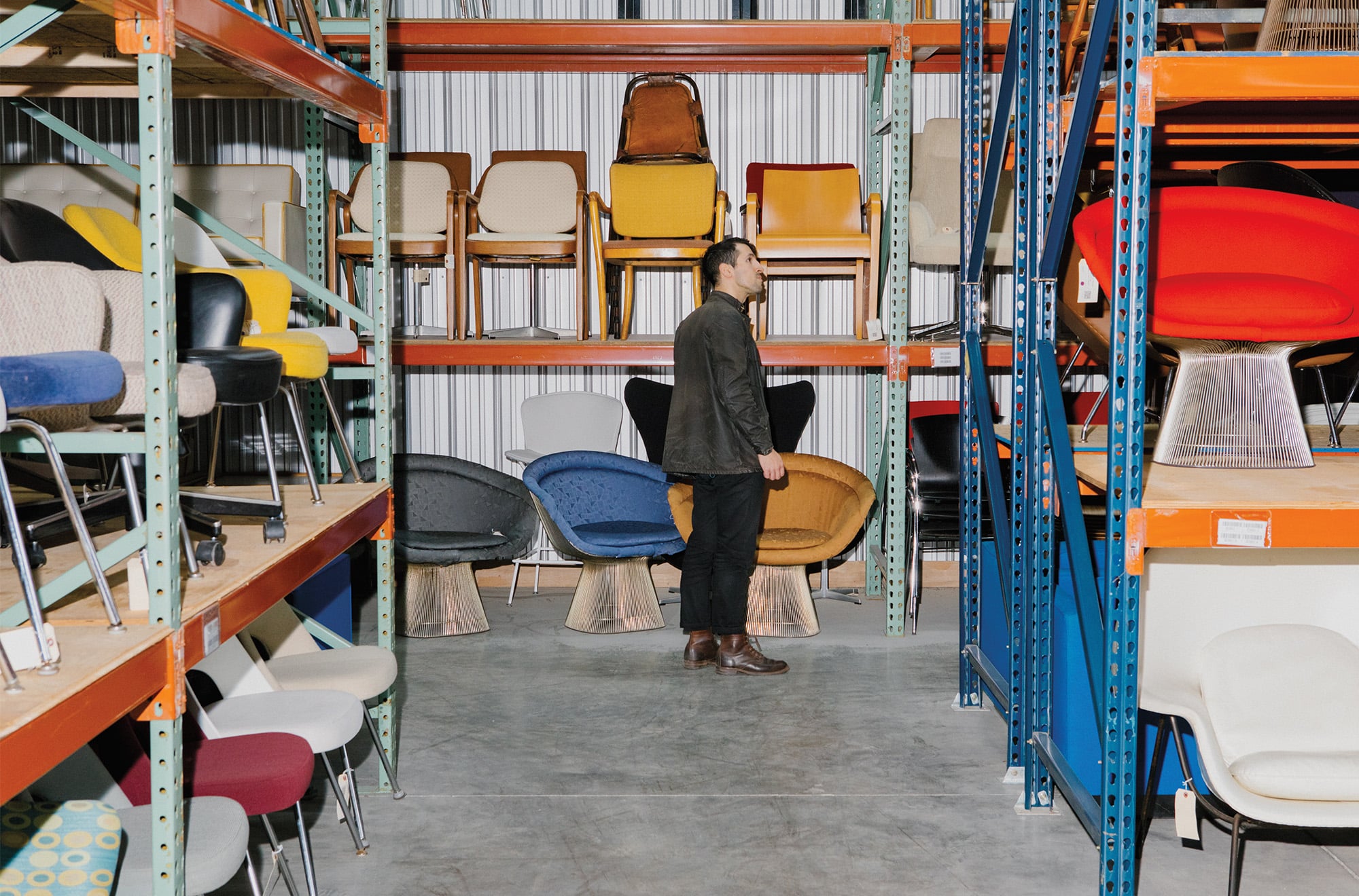 cofounder walking through the long aisles of the warehouse with reclaimed and refurbished chairs on all shelves and floor. 
