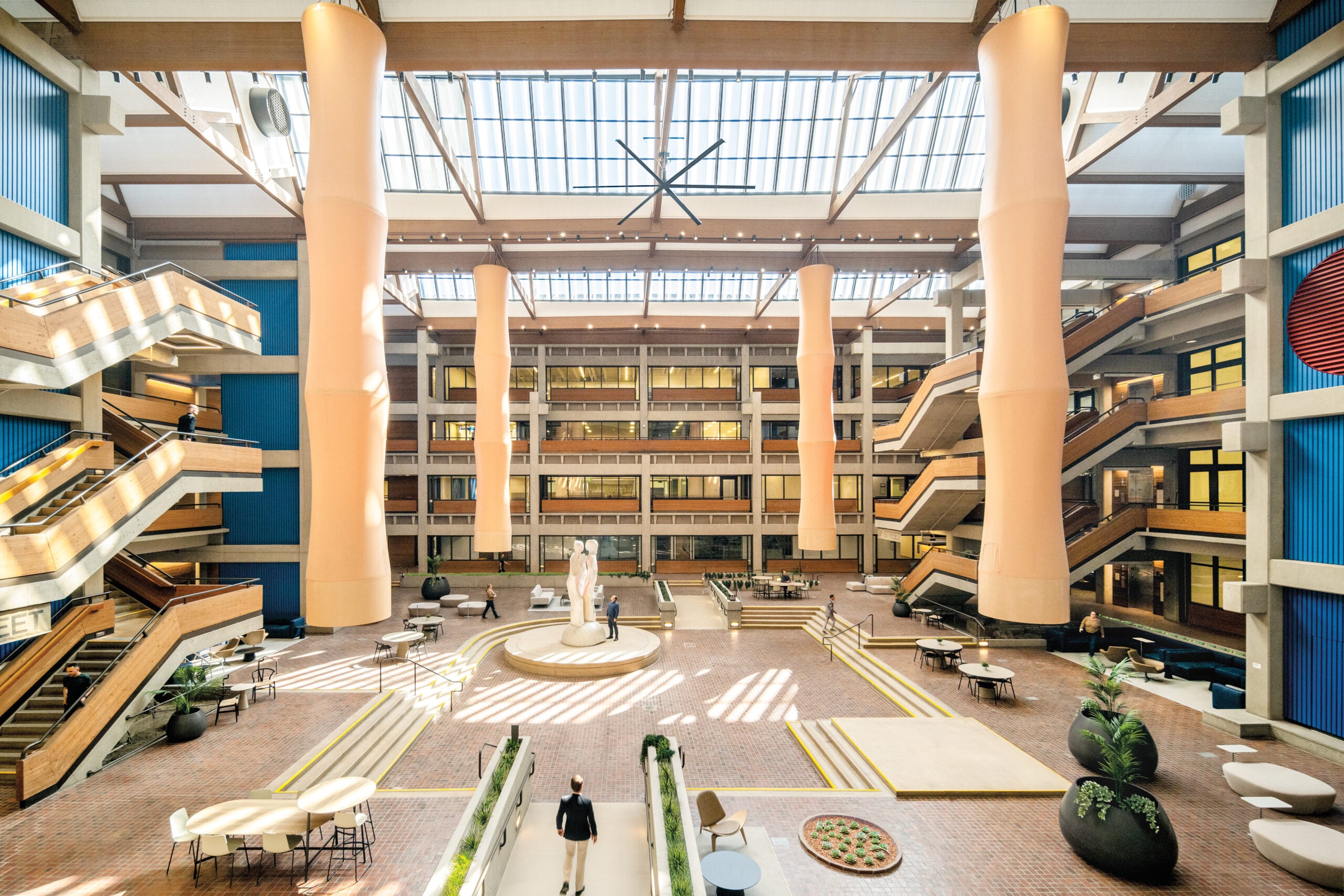 A modern, daylight-filled foyer inside the Bateson Building featuring large orange fans hanging from the ceiling, blue acoustic wall panels and flexible seating.