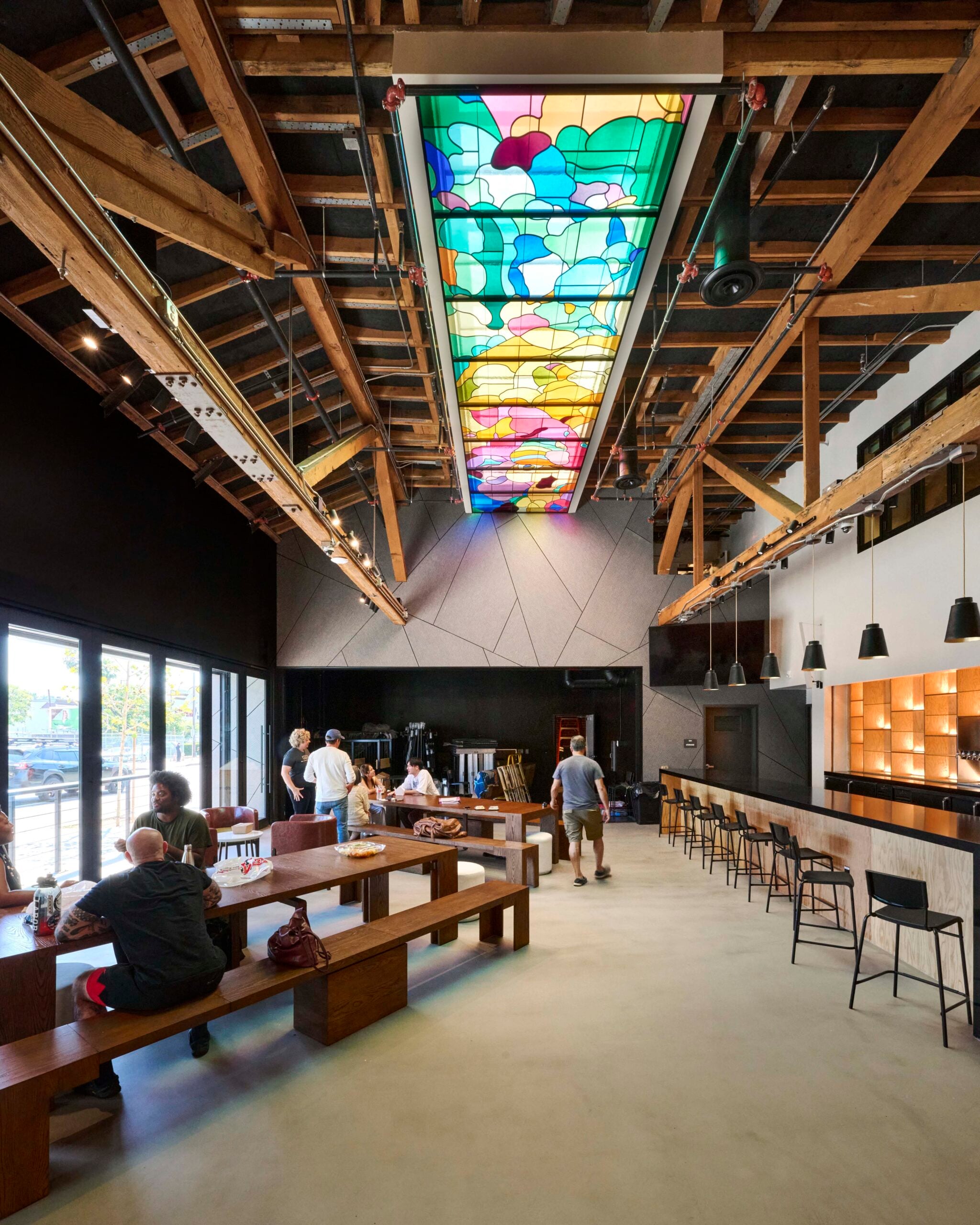 A perspective view of the theatre lobby/lounge area, highlighting the polished concrete floors and brick accent wall. The image shows the long bar on the left, hanging pendant lights, and the intricate wooden ceiling structure above.