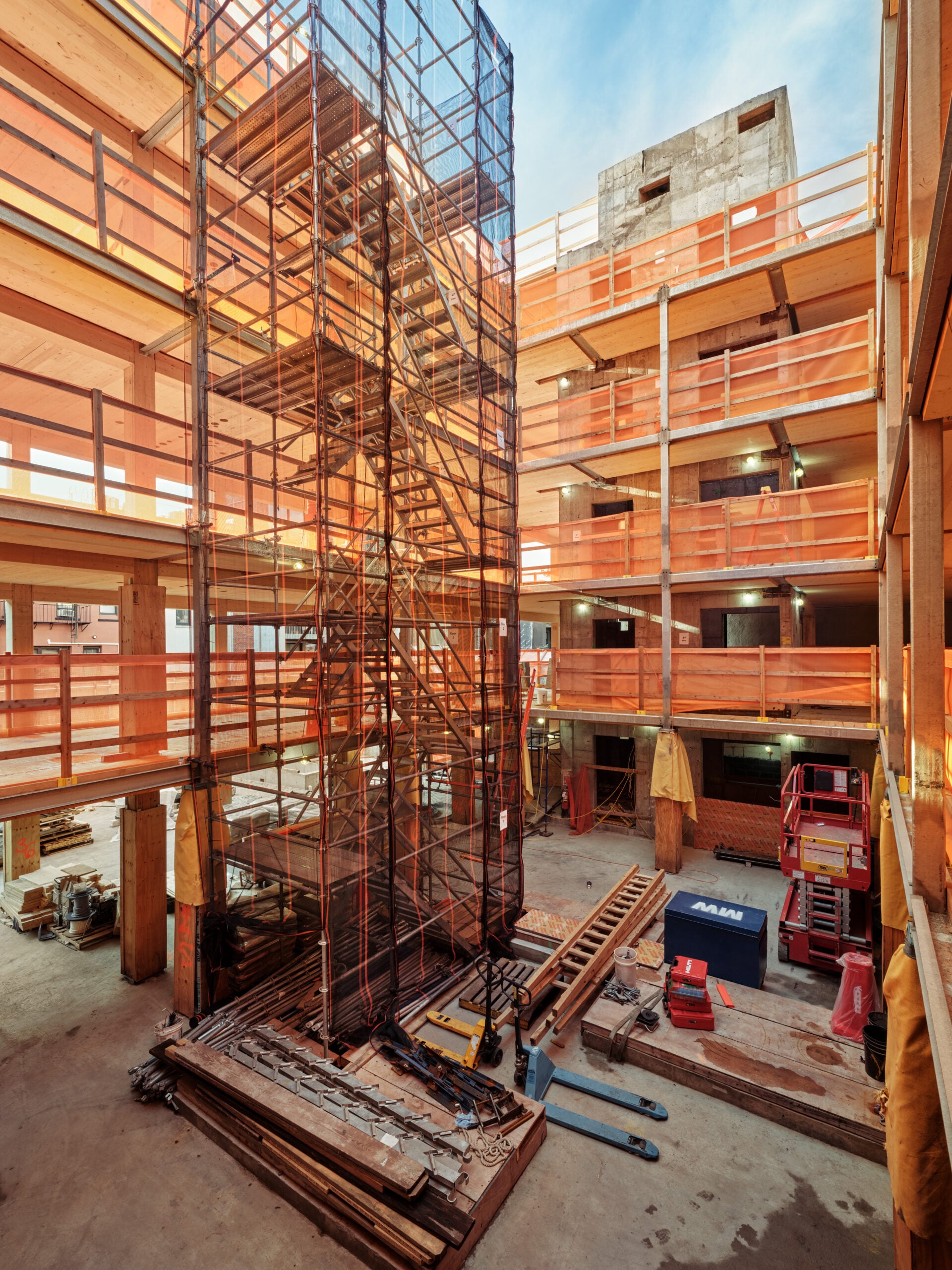 A view inside the courtyard during the construction phase, showing the steel framework for the spiral staircases and elevator shaft rising amidst the timber building structure.