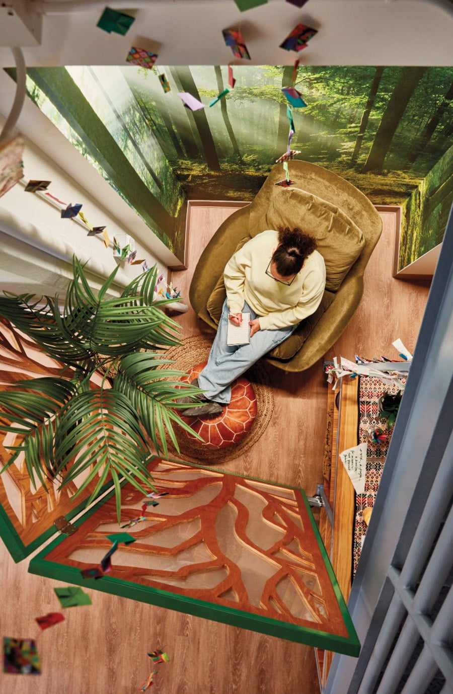 Birds-eye view of a cozy corner with a velvet chair, partition screen, potted plant and forest wallpaper.