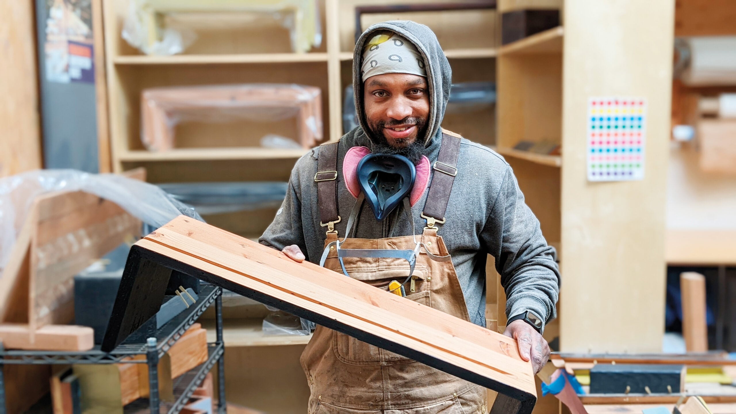 Workshop for upcycled furniture with a figure showing a plank of wood, cabinetry in the background.