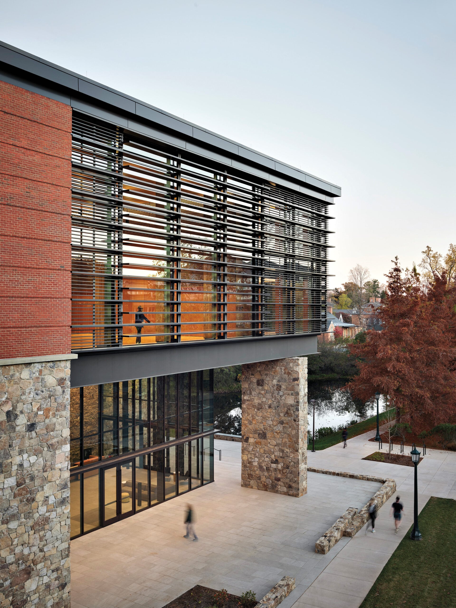 University of Virginia Contemplative Commons exterior featuring stone pathways next to a pond, a modern brick facade with large glass windows and walls