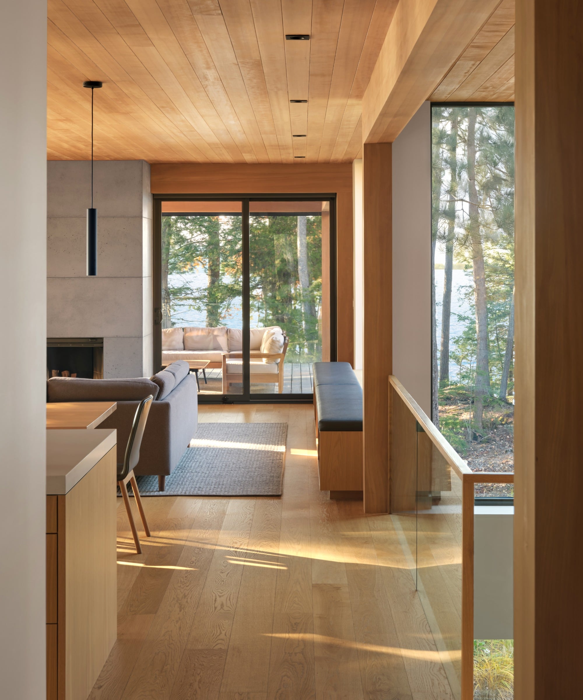 Wood Muskoka cottage interior with glass windows and trees visible in the distance.