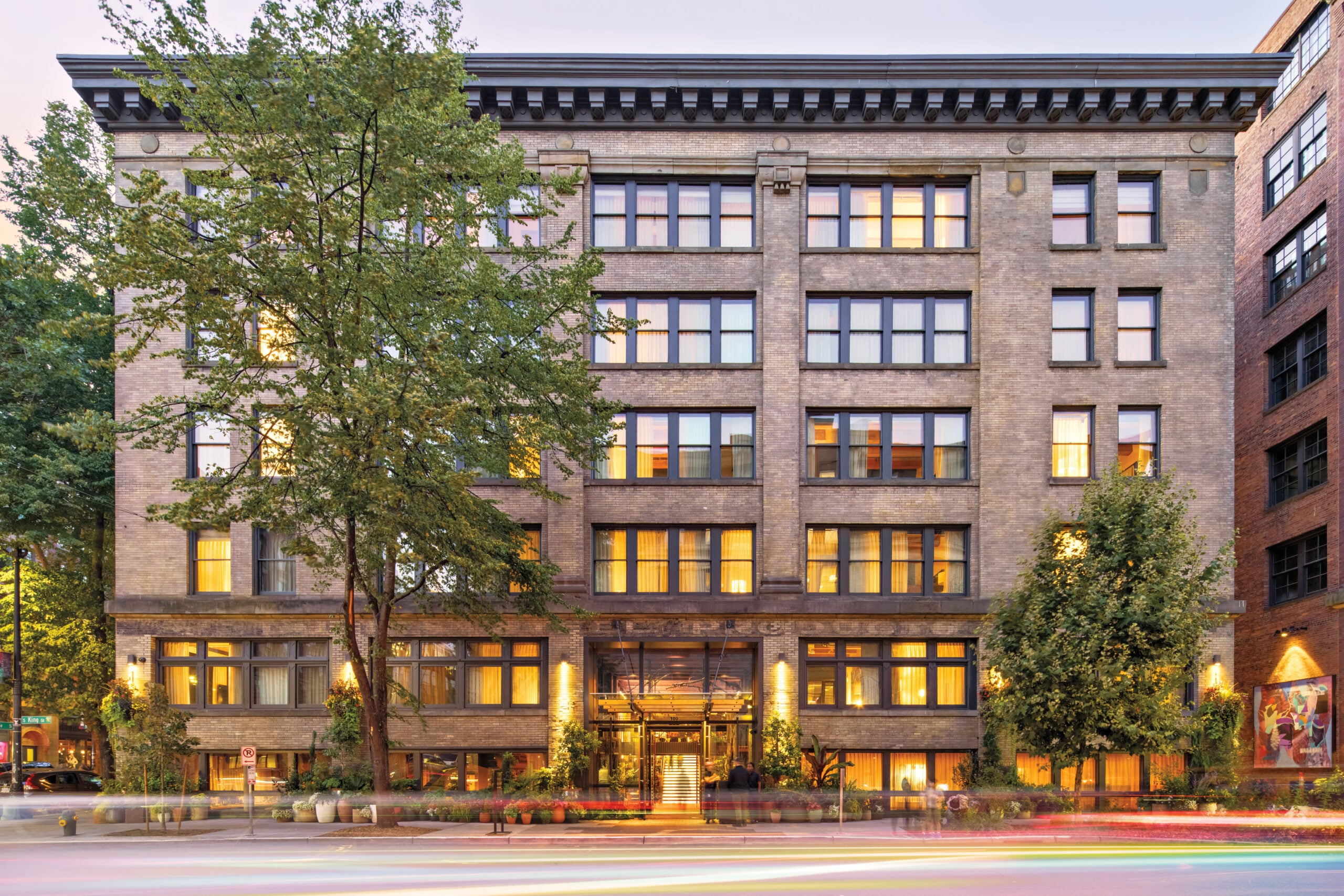 Hotel exterior view from the street, with reopened boxcar loading doors, brick facade and trees on sidewalk