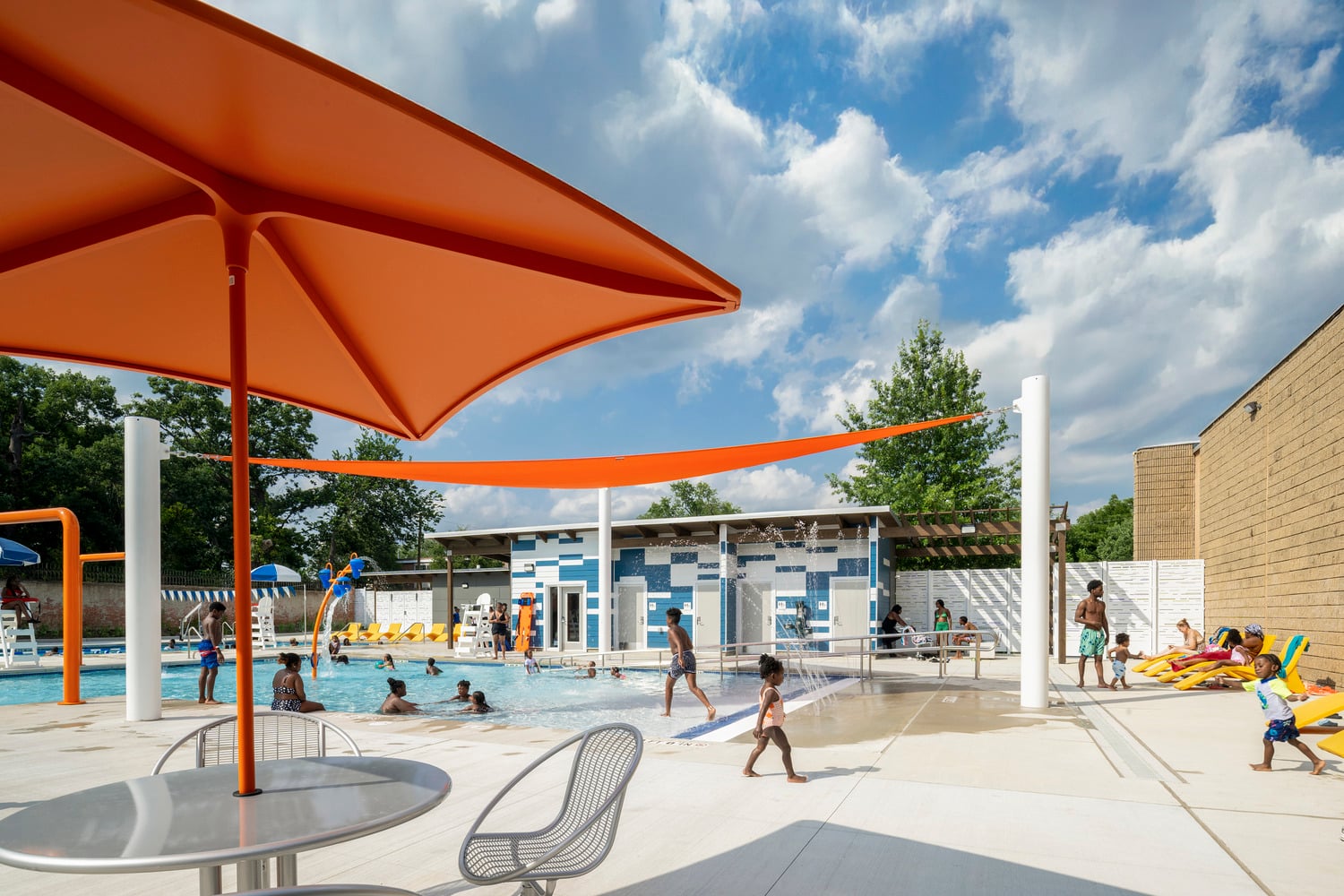 Outdoor swimming pool with bright orange umbrella and orange accents, full of people
