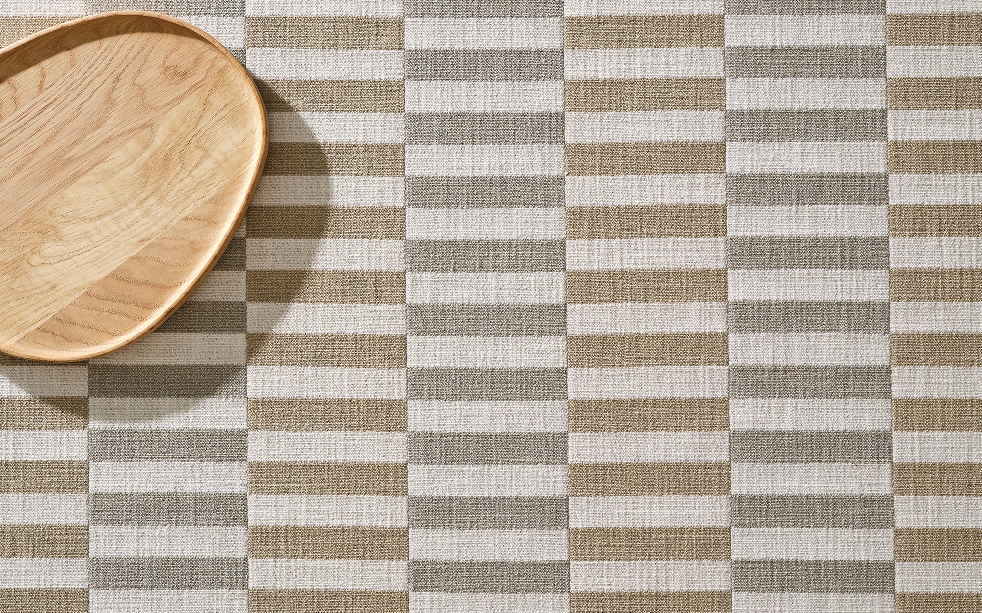 A wooden oval plate sits on a beige and white checkered fabric surface with a woven texture.