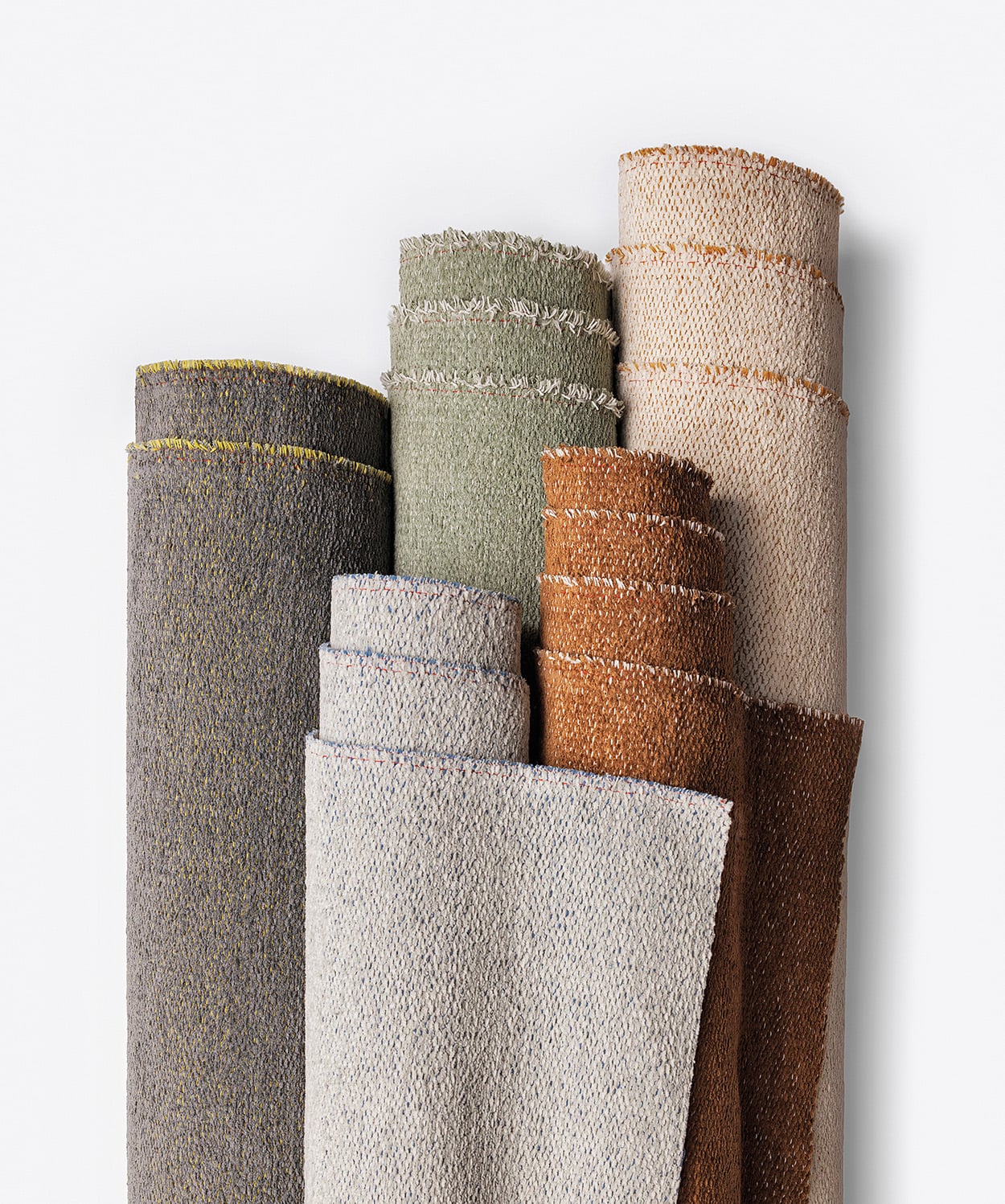 Five rolls of textured fabric in shades of gray, green, beige, and brown are arranged vertically against a plain white background.