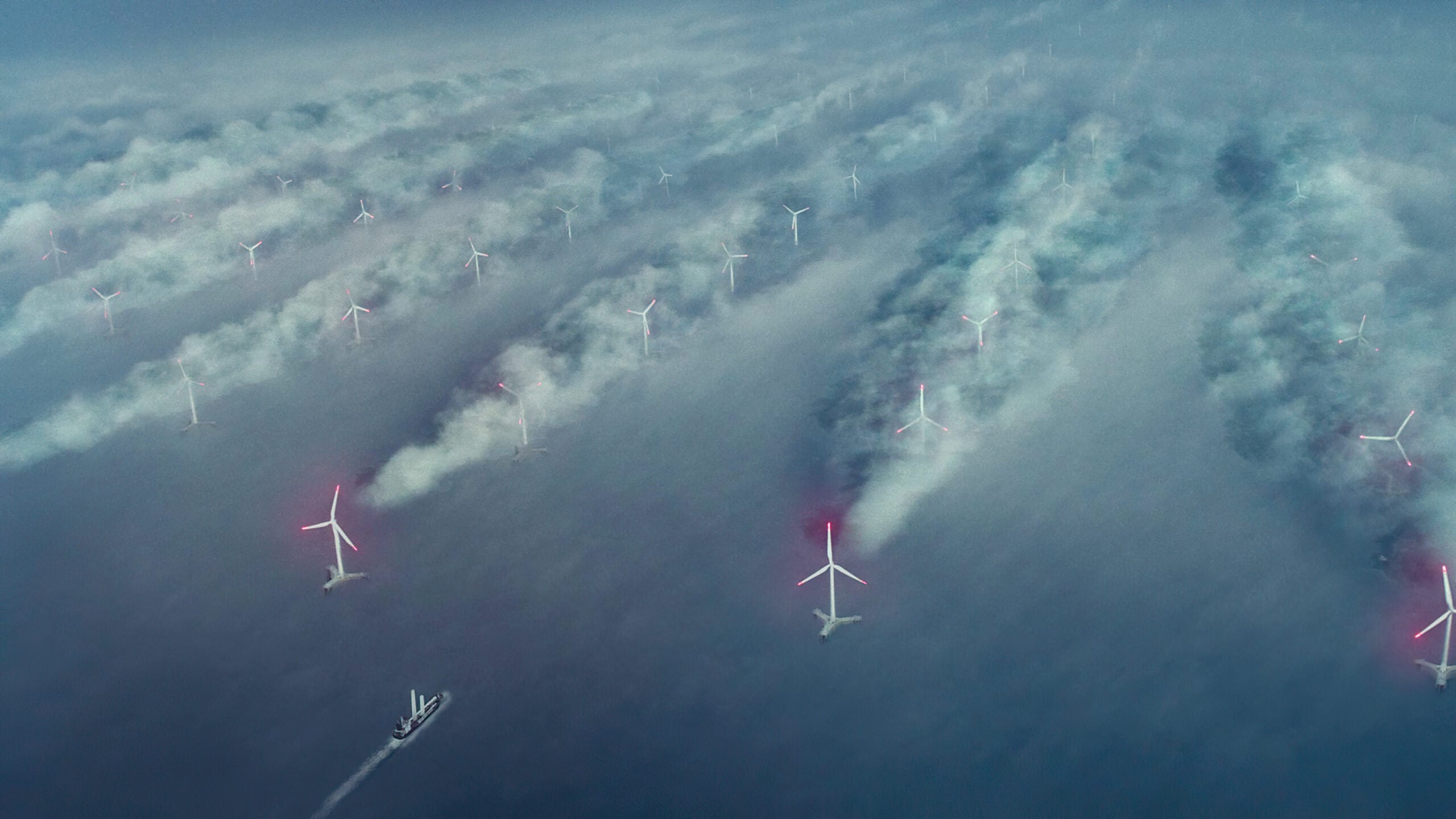 Offshore wind turbines emerging through misty clouds over the ocean, with a small ship passing below.