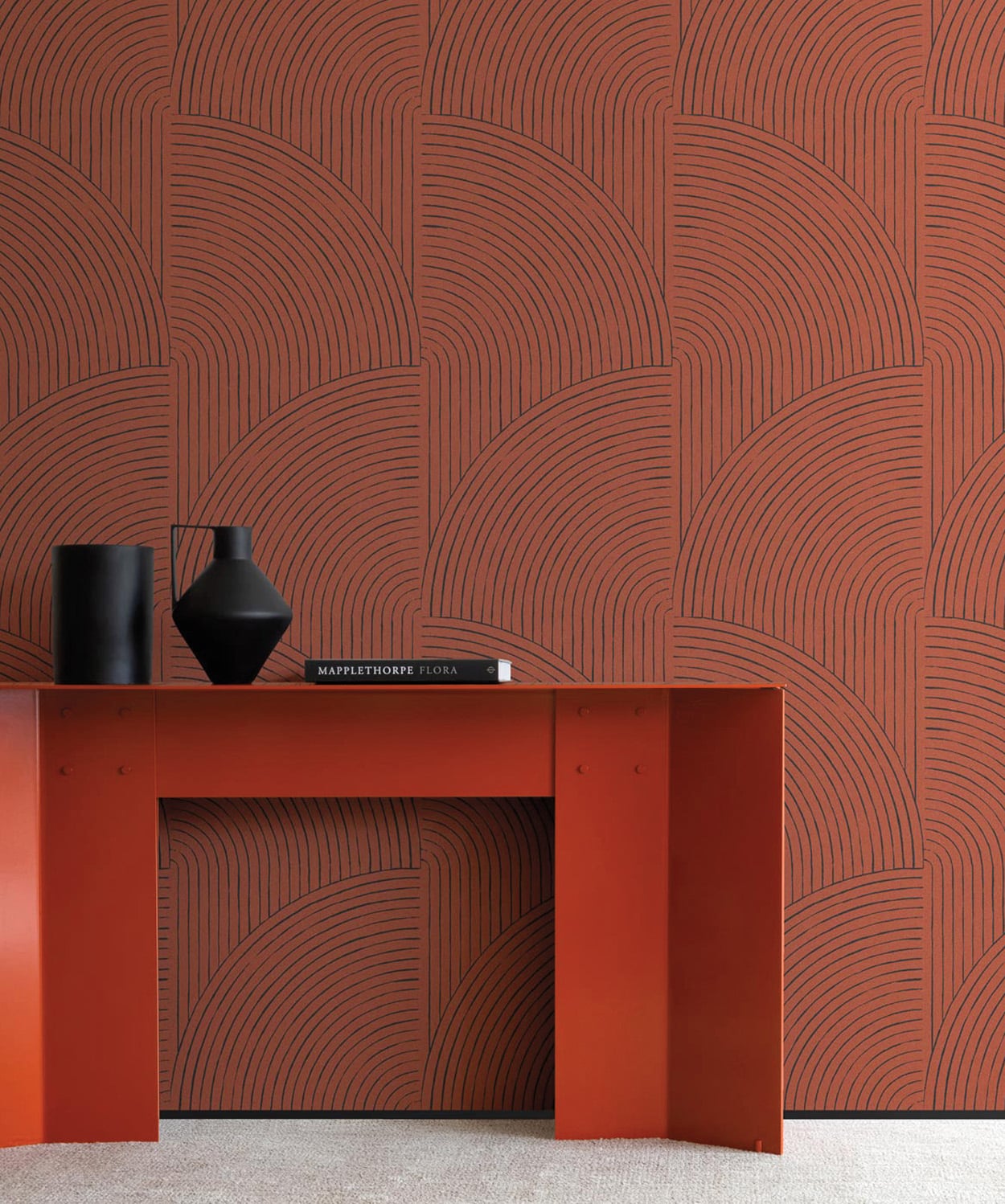 A modern orange desk with two black vases and a book sits against a patterned wall with geometric, curved line designs in shades of orange and brown.