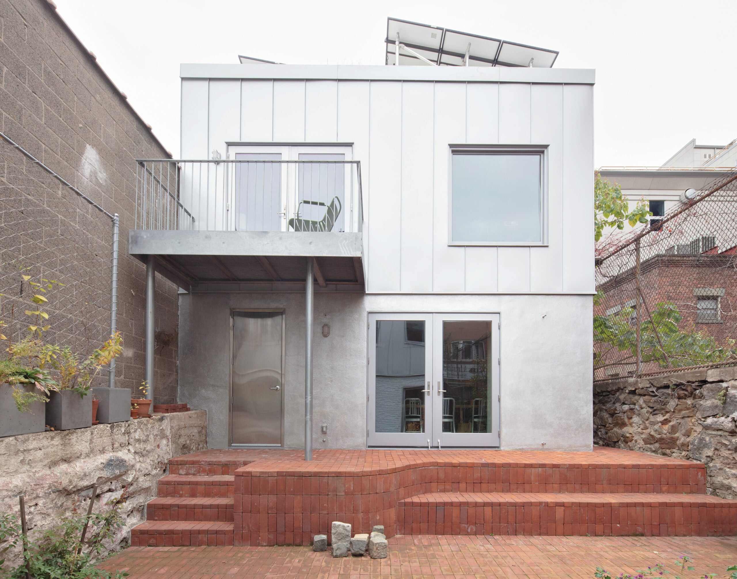 A building with a galvanized steel facade, brick landscaping and some potted plants