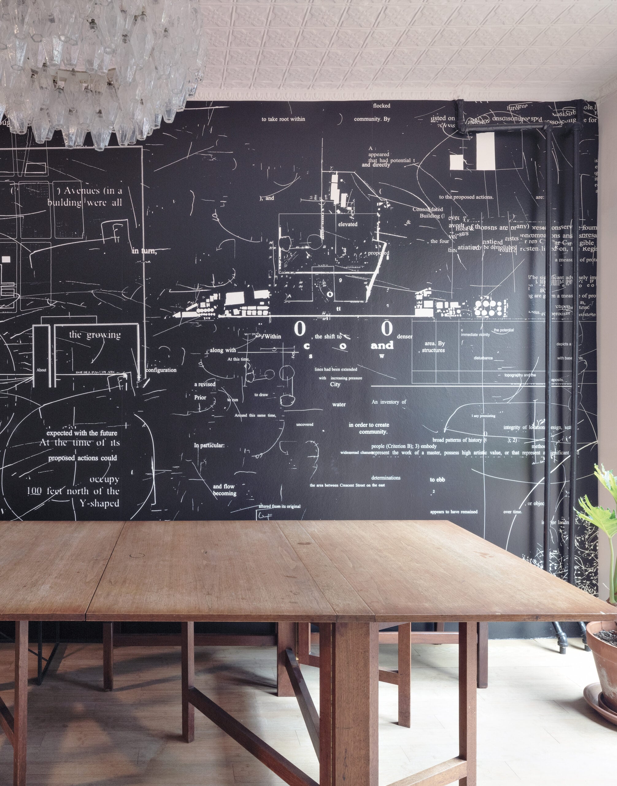 Black wall with white diagrams, writing and other symbols behind a wood table.