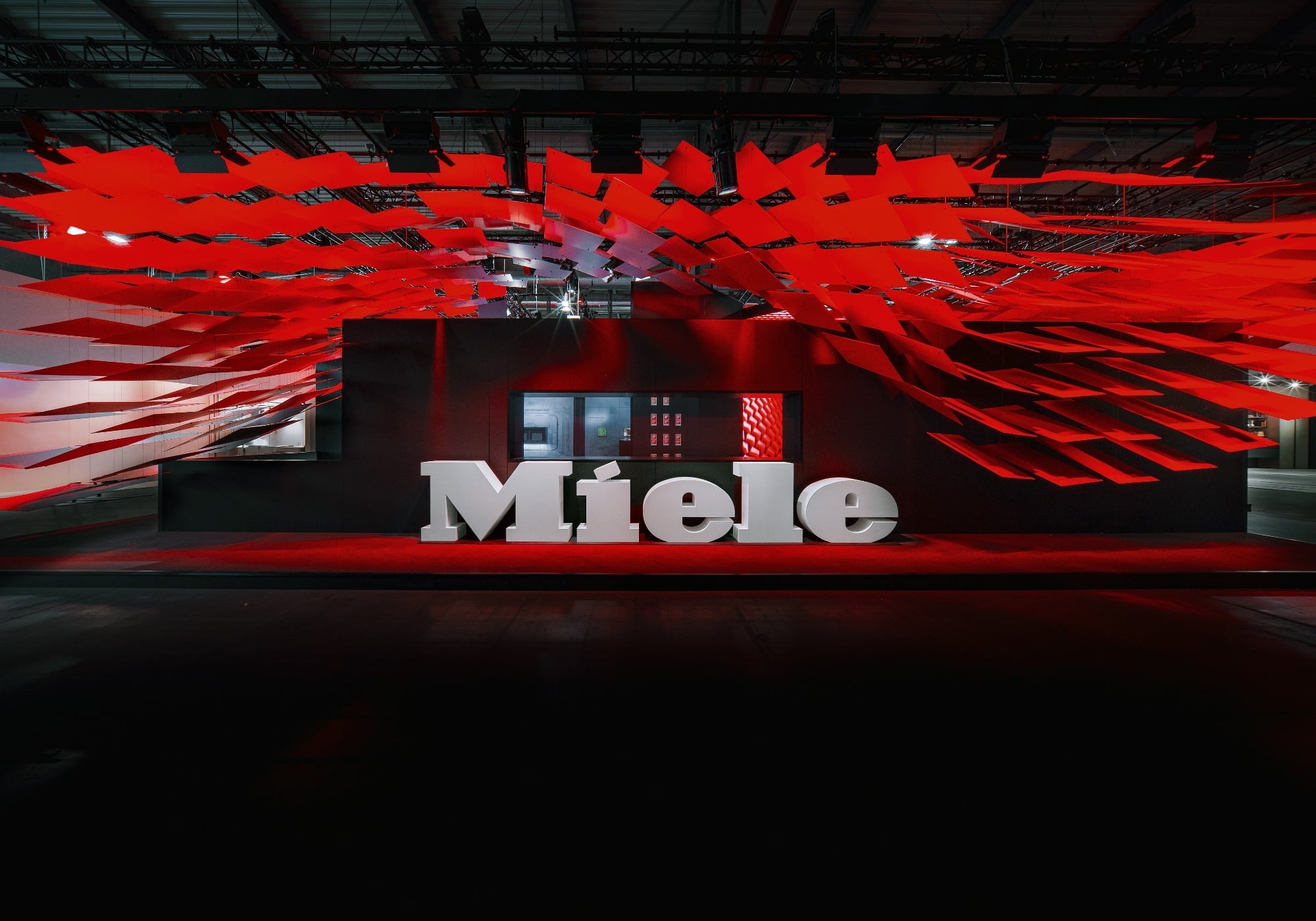 Large white "Miele" letters stand in front of a black structure with red geometric decorations, creating a dramatic, modern display at Milan Design Week and highlighting the brand’s commitment to sustainable products.