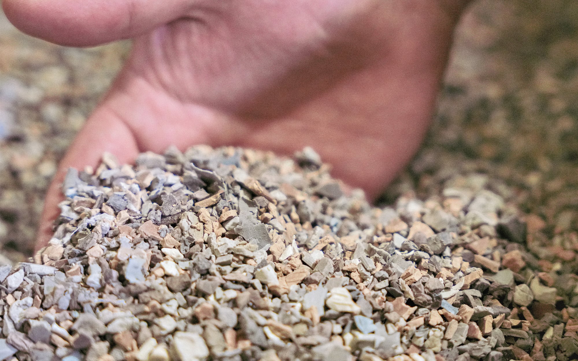 A hand holds a pile of small, light-colored gravel, showcasing the material's texture and composition.