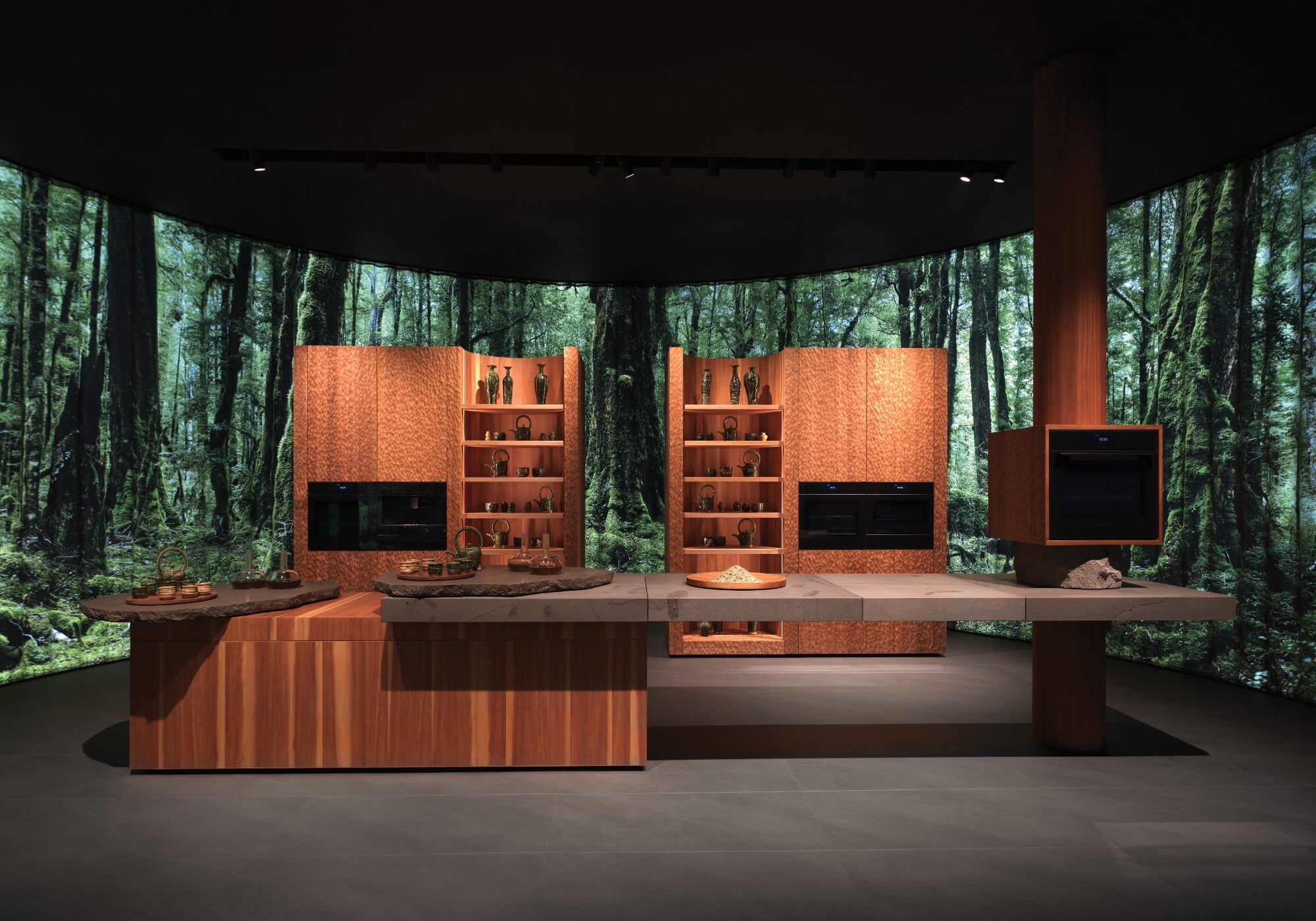 Modern kitchen with wood cabinets, open shelving, and built-in appliances, set against a panoramic forest backdrop on curved walls—an inspiring nod to Milan Design Week sustainable products.