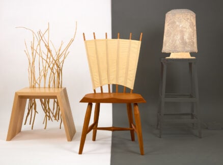 Three artistic chairs are displayed: one with vertical wooden sticks, one with a fan-like backrest, and one featuring textured textiles on a lampshade atop a tall stool, against a split white and gray background.