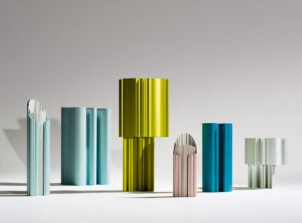 Six colorful, vertically standing sculptural objects with ribbed, cylindrical shapes are arranged on a flat surface against a neutral background, evoking the innovative design spirit showcased at ICFF.