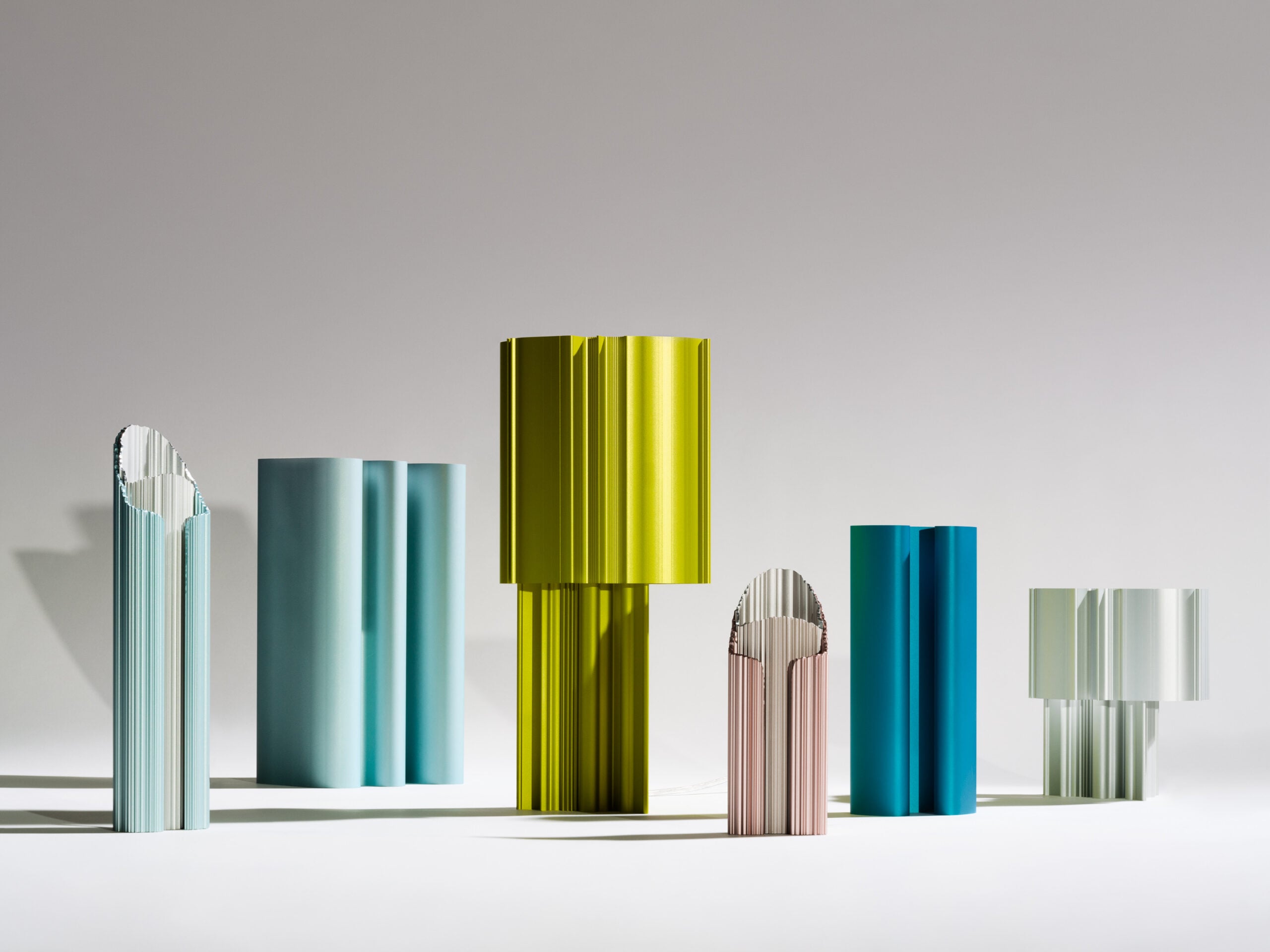 Six colorful, vertically standing sculptural objects with ribbed, cylindrical shapes are arranged on a flat surface against a neutral background, evoking the innovative design spirit showcased at ICFF.