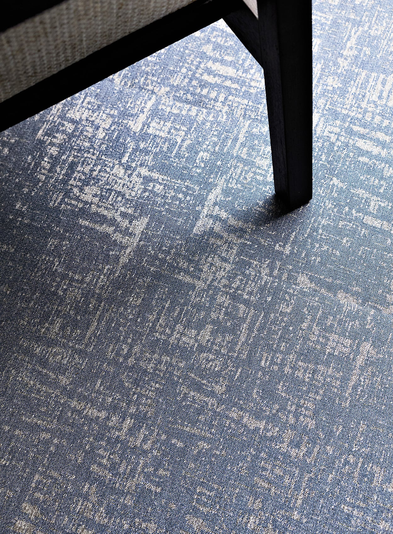 Close-up of a chair leg, showcasing the material detail, on a blue and light gray patterned carpet.