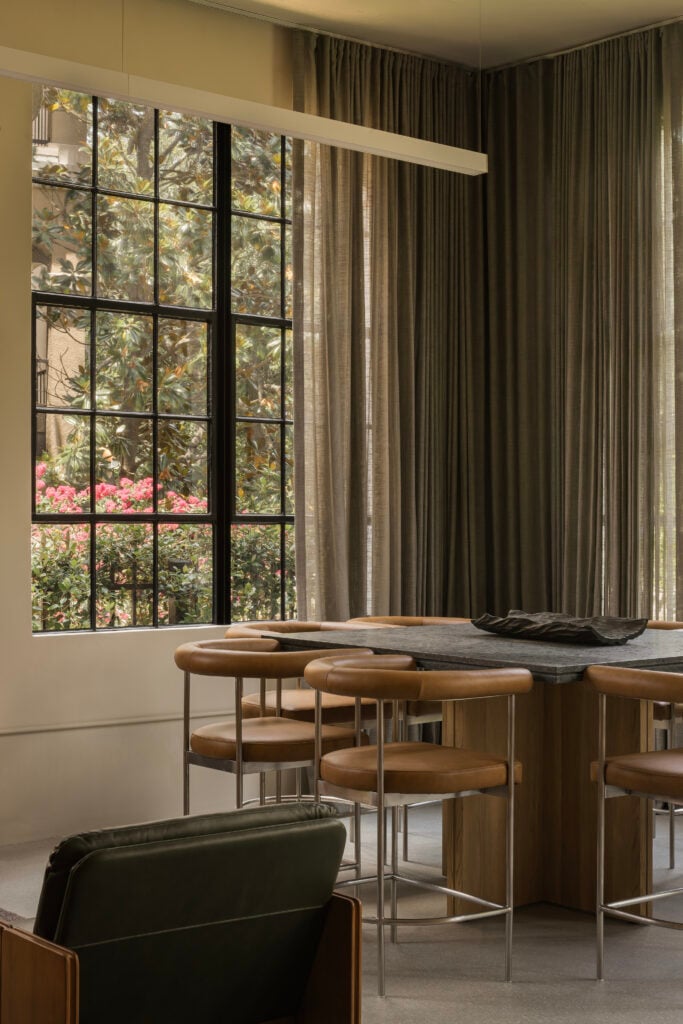A modern dining area with brown leather chairs around a wooden table by BLDUS, featuring large windows and floor-to-ceiling curtains that let in natural light.