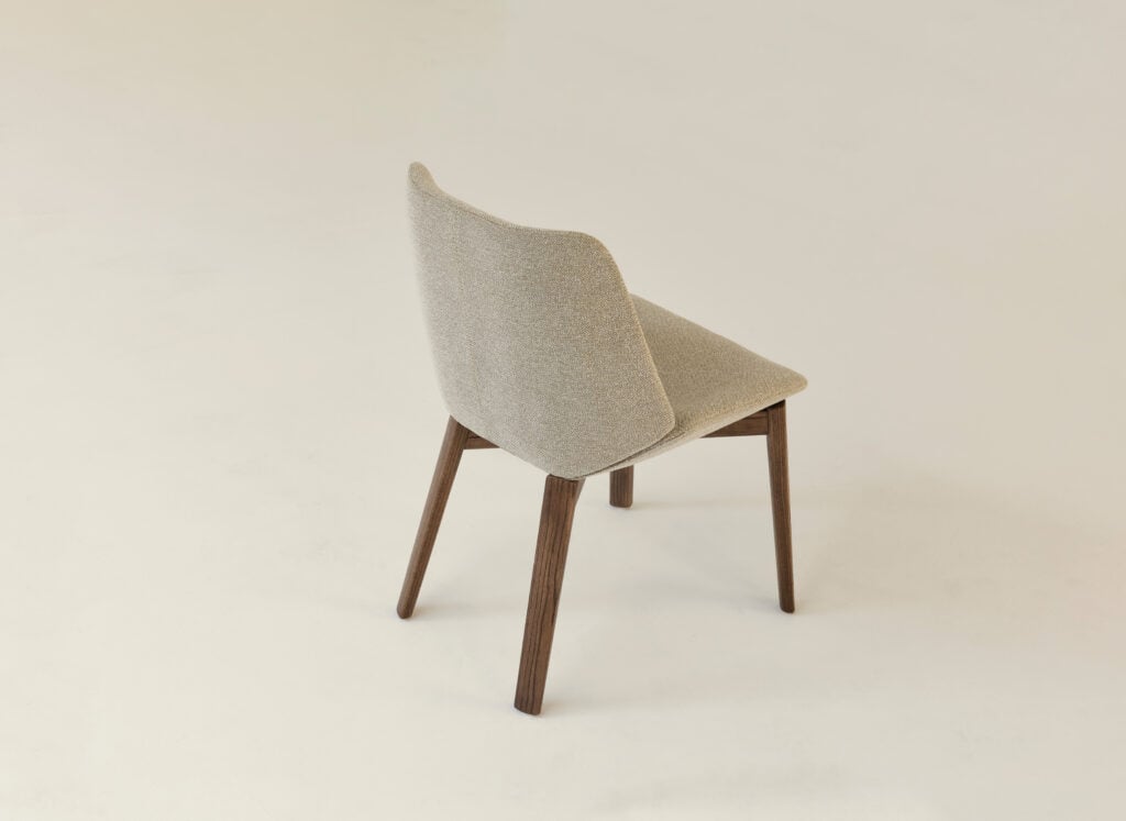 A beige upholstered chair with wooden legs is positioned at an angle on a plain light background, adding a touch of METROPOLISLikes modern elegance.