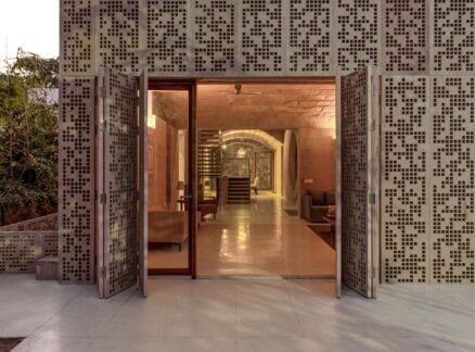 Entrance with open glass doors framed by perforated stone panels, revealing a modern interior with elegant stone arches, comfortable seating, and warm lighting.