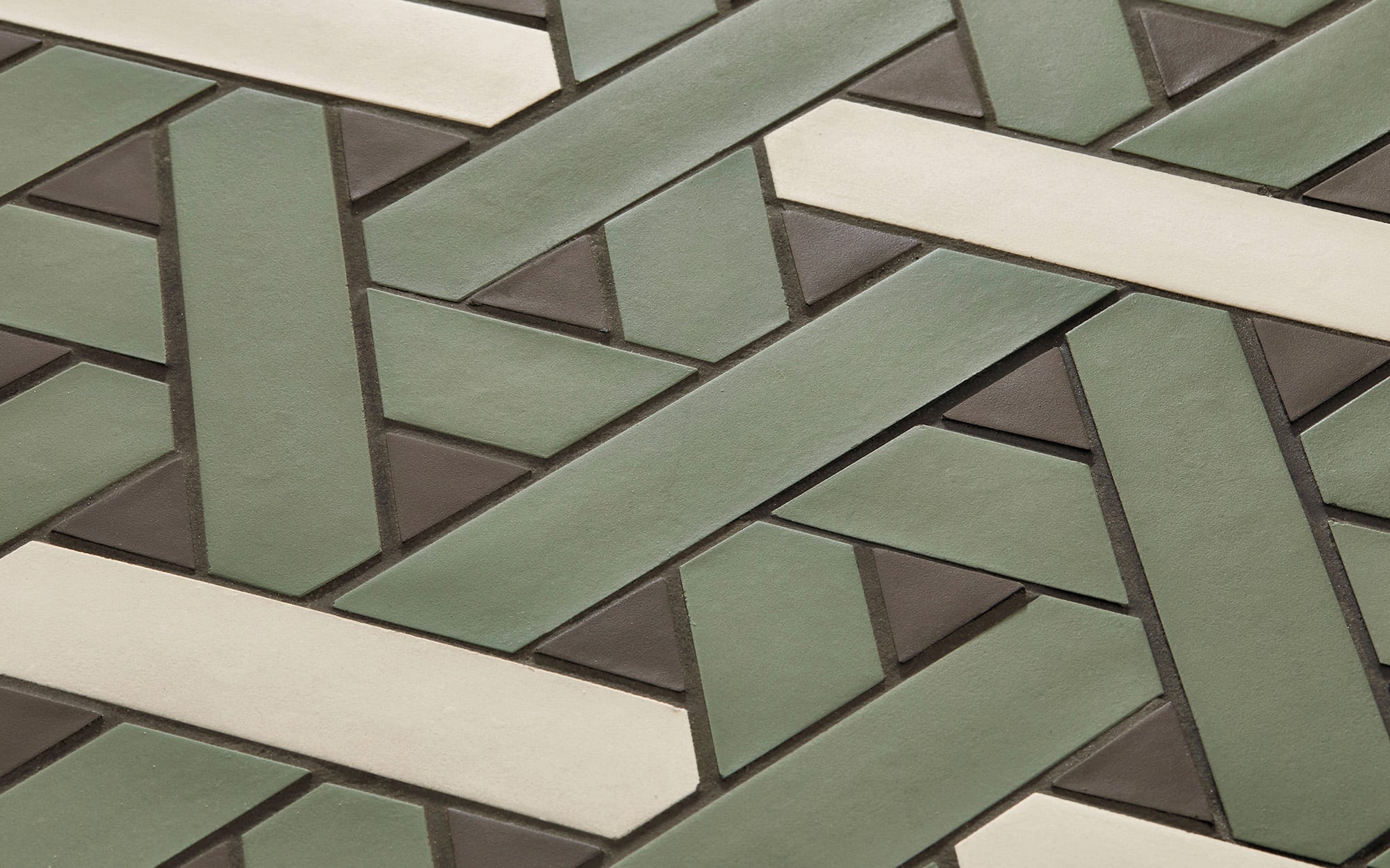 Close-up of a geometric tile pattern featuring green, beige, and dark brown rectangular tiles arranged in an interlocking design.