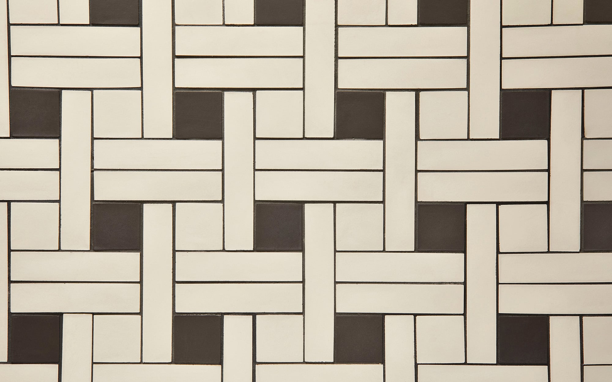Alternating light and dark rectangular tiles arranged in a woven basketweave pattern on a flat surface.