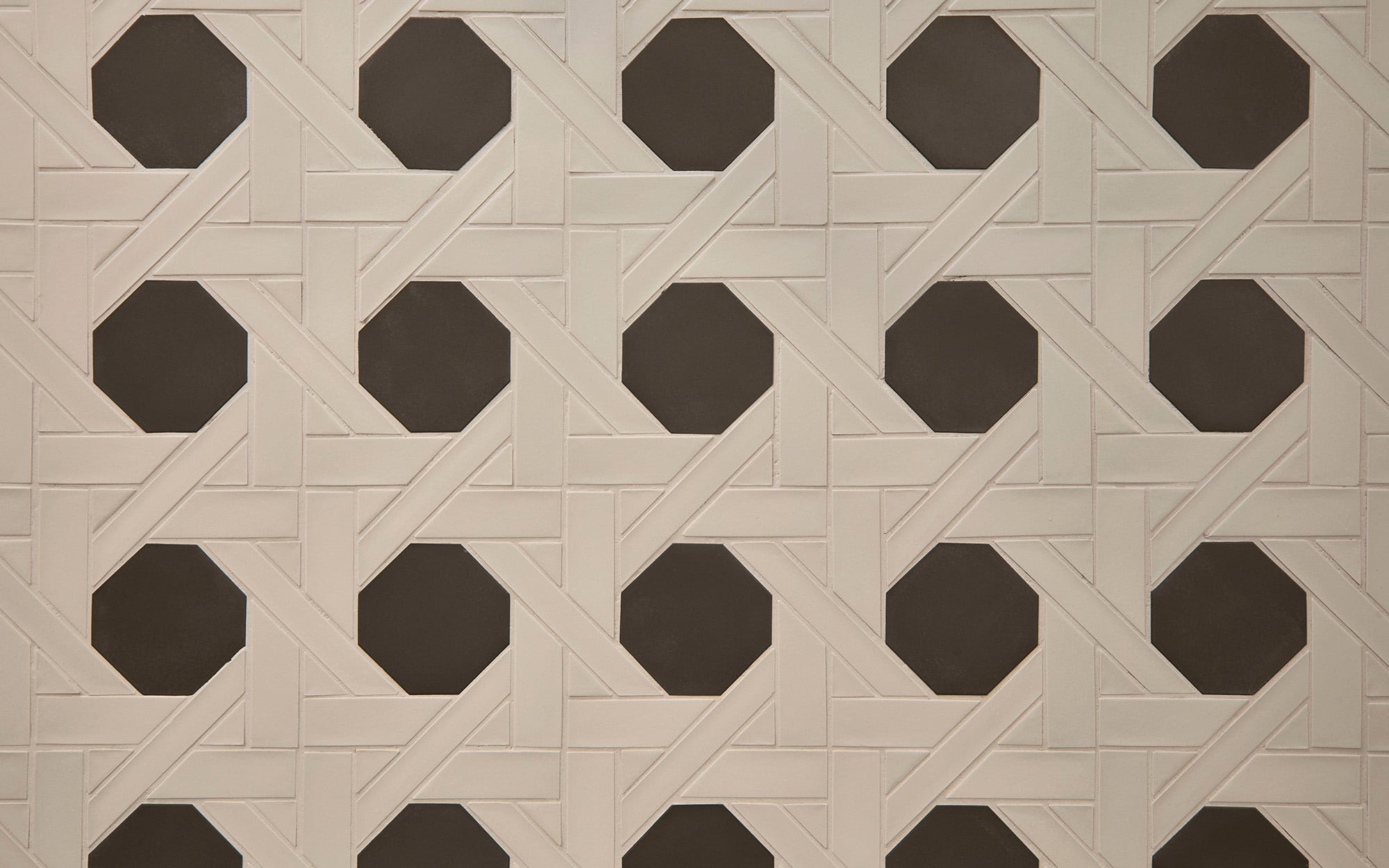 Geometric patterned wall with interlocking cream-colored tiles forming diamond shapes around black octagonal tiles.