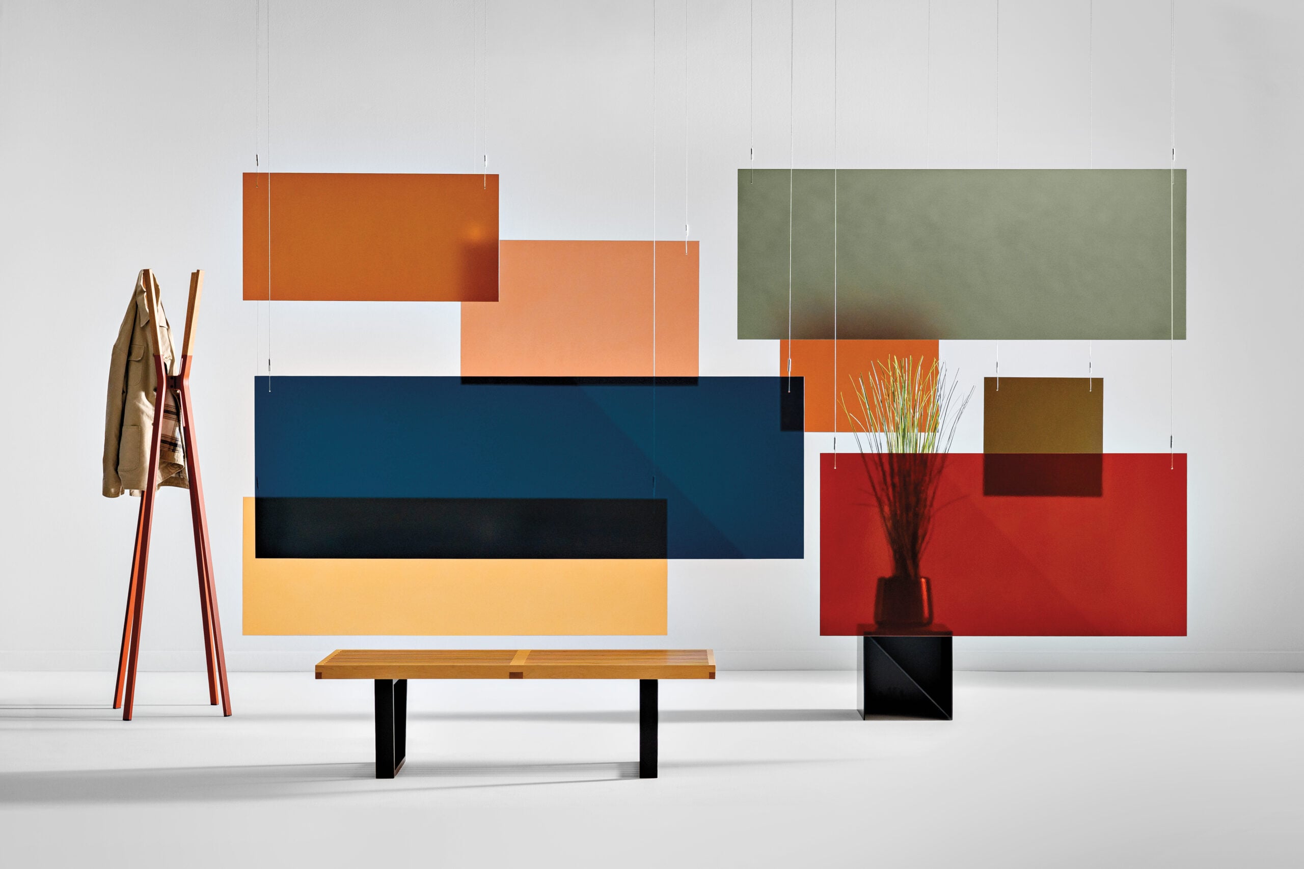A minimalist room with colored rectangular panels hanging from the ceiling, a wooden bench, a coat rack with a jacket, and a vase with tall grass on a black stand—perfect for fans of METROPOLISLikes.