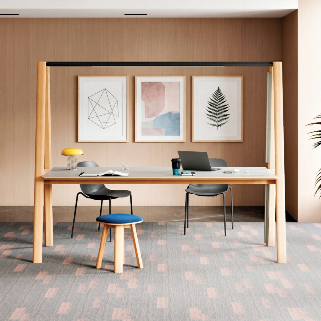 A desk with a laptop, coffee cup, and notebook sits in a room with three framed pictures on the wall, capturing a scene METROPOLISLikes for its modern simplicity.