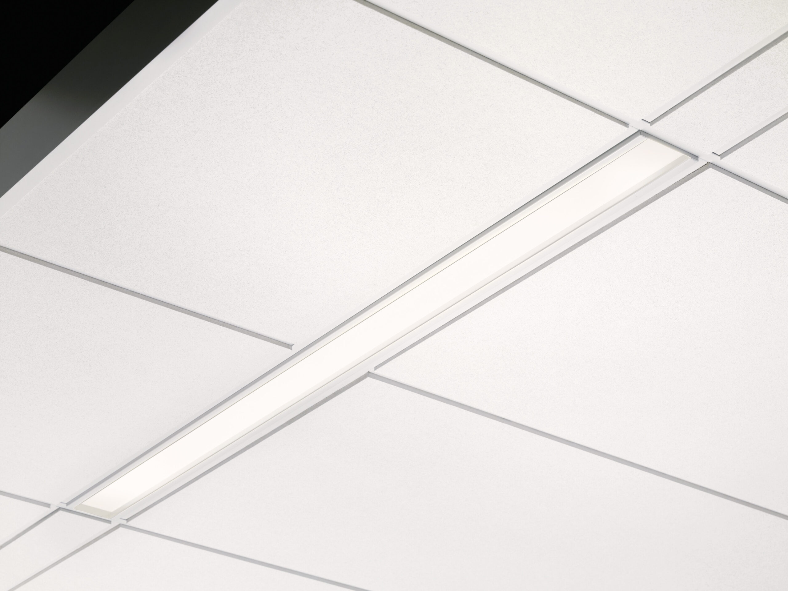 A recessed linear light fixture is installed in a white drop ceiling with gridlines.